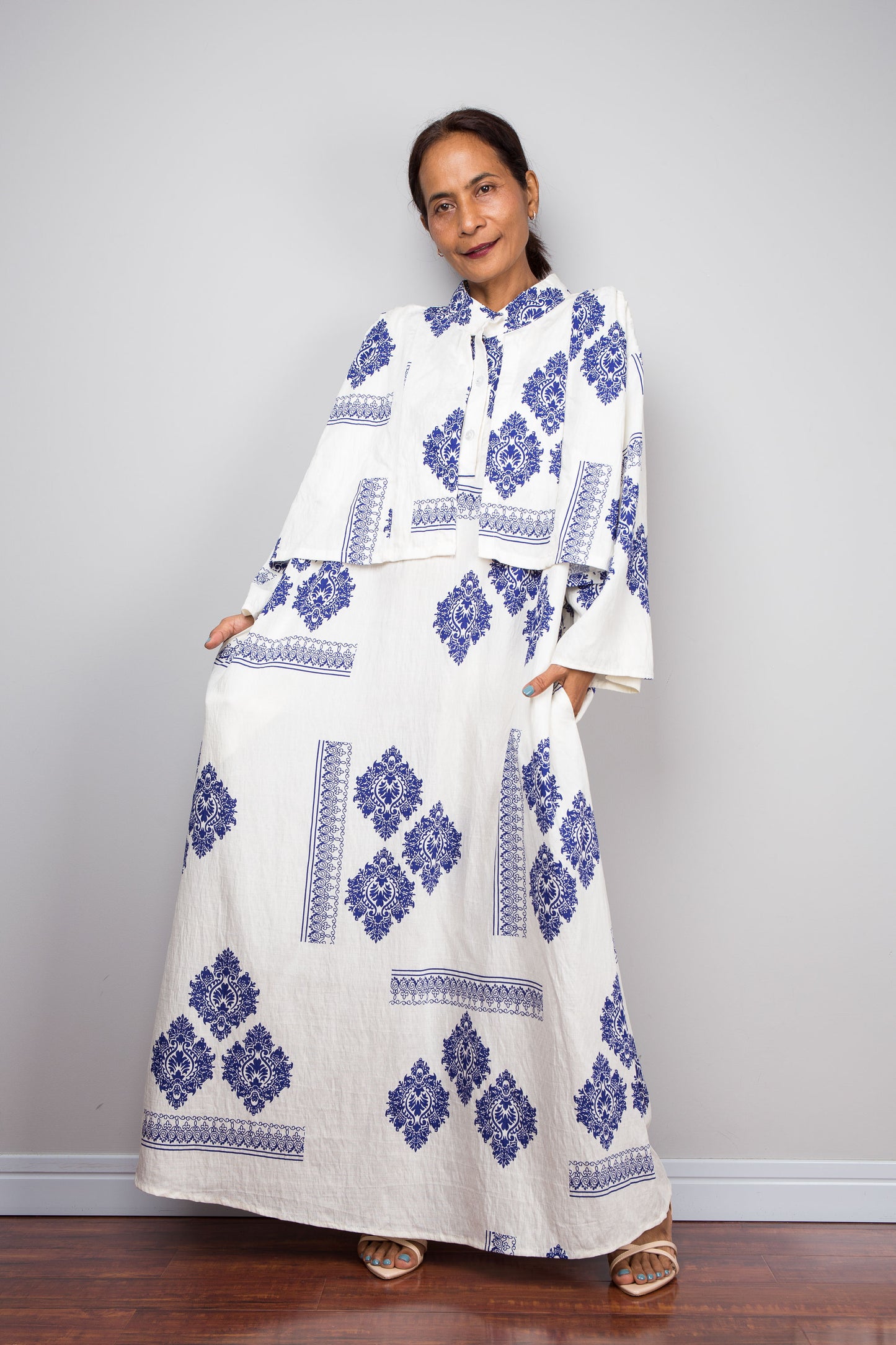 Front view of a model wearing the Nuichan white and blue medallion kaftan dress while lifting the lower skirt part, displaying the full body of the dress beneath with diamond medallion print and decorative border banding