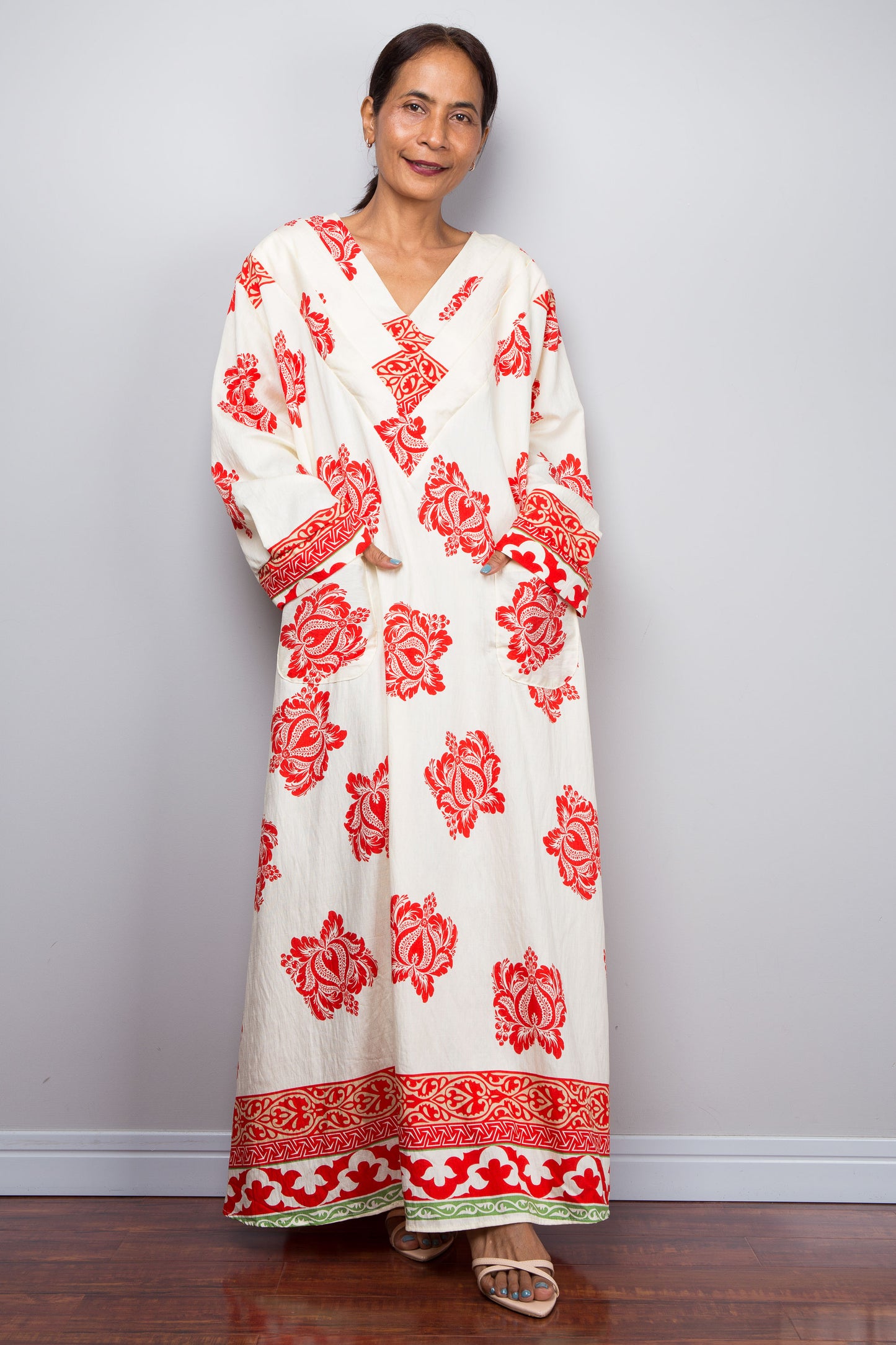 Woman wearing a white caftan dress with red floral patterns against a plain background