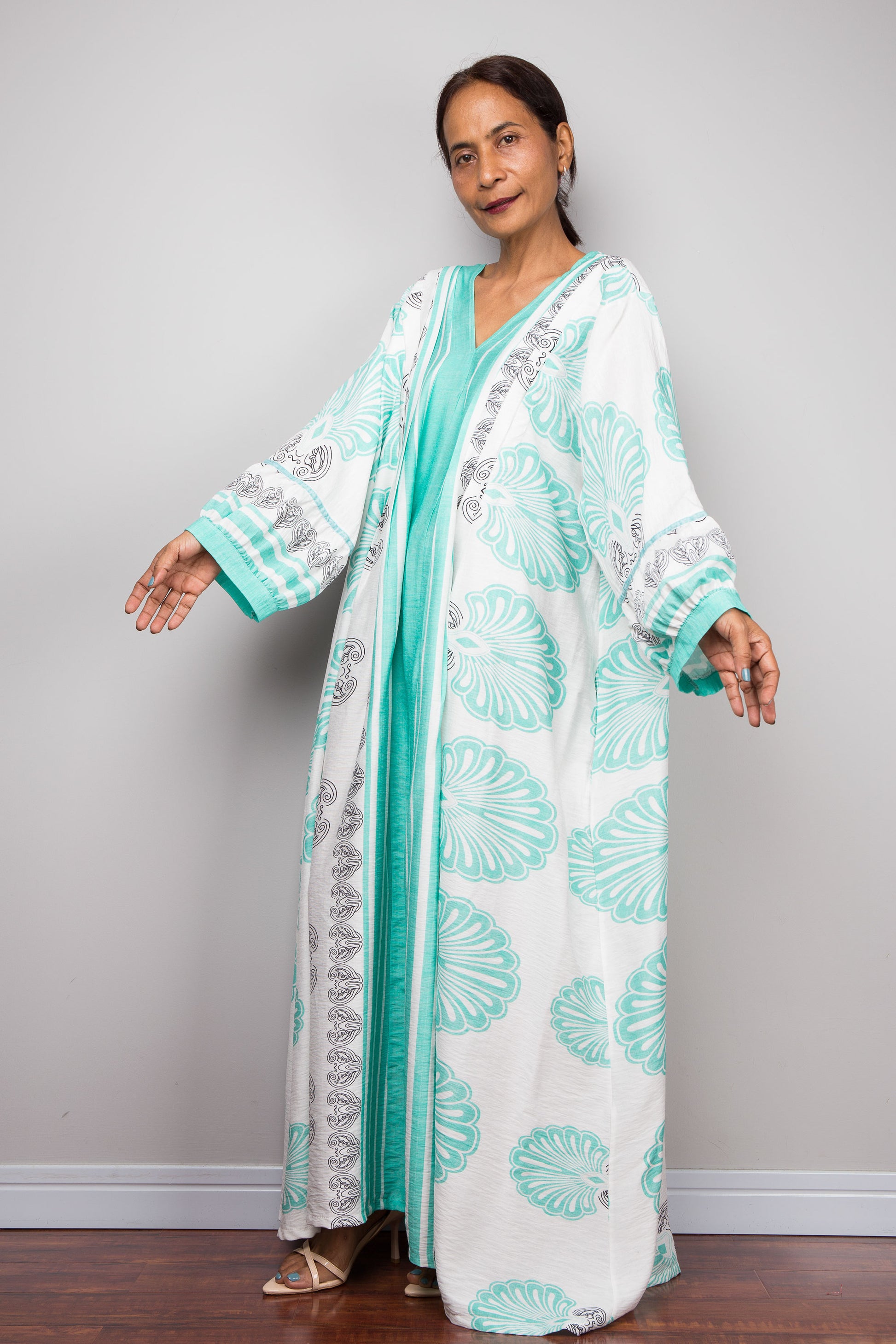 Full-length side on view studio shot of a petite model wearing the Nuichan bohemian caftan dress in mint green and white, highlighting the vertical-striped paneling, deep V-neckline, and functional side pockets.