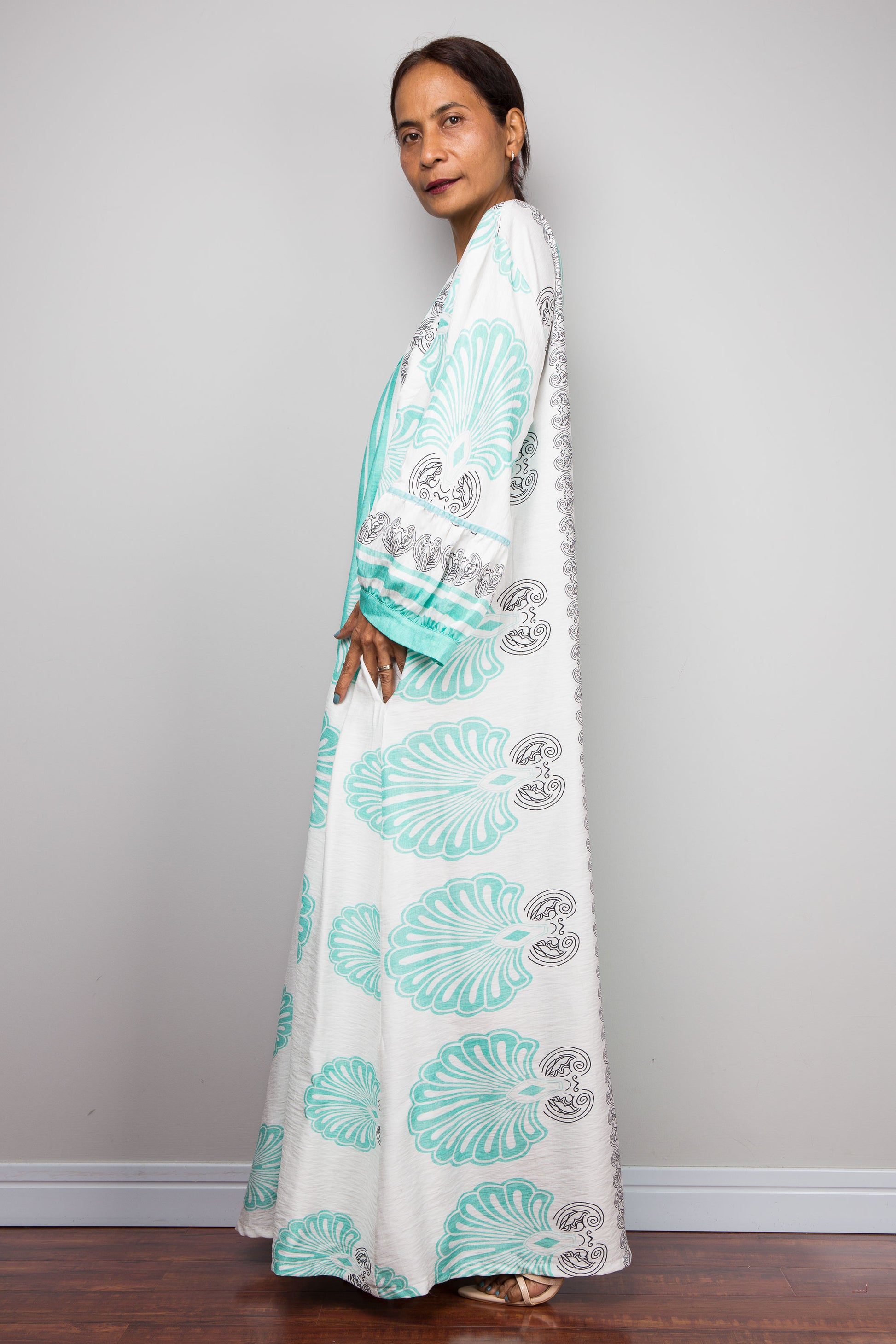 Side view studio shot of a model wearing the Nuichan bohemian caftan dress in mint green and white, highlighting the vertical-striped paneling, V-neckline,and functional side pockets.