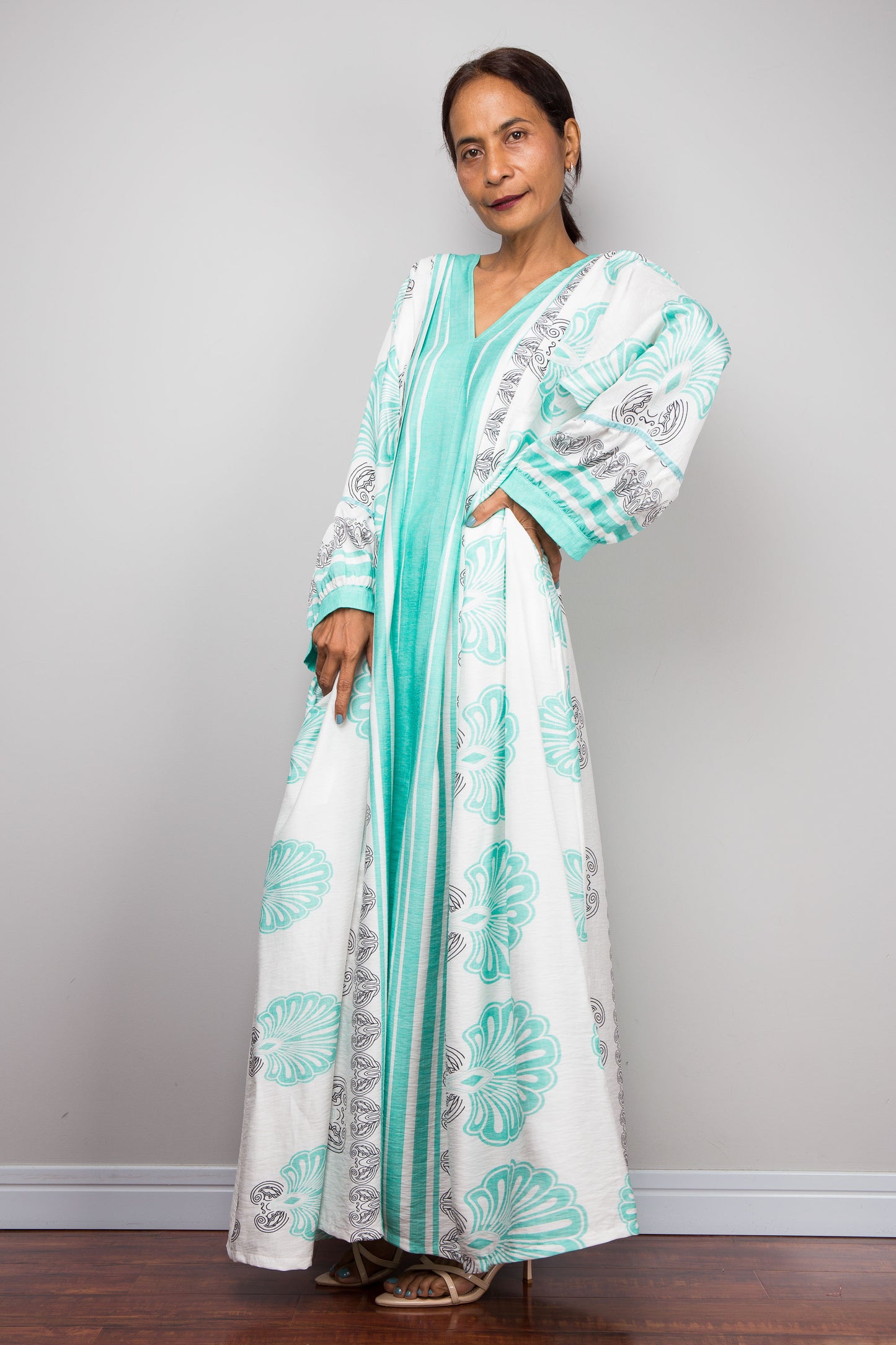 Image of a model wearing the Nuichan bohemian caftan dress in mint green and white, highlighting the vertical-striped paneling, V-neckline,and functional side pockets.