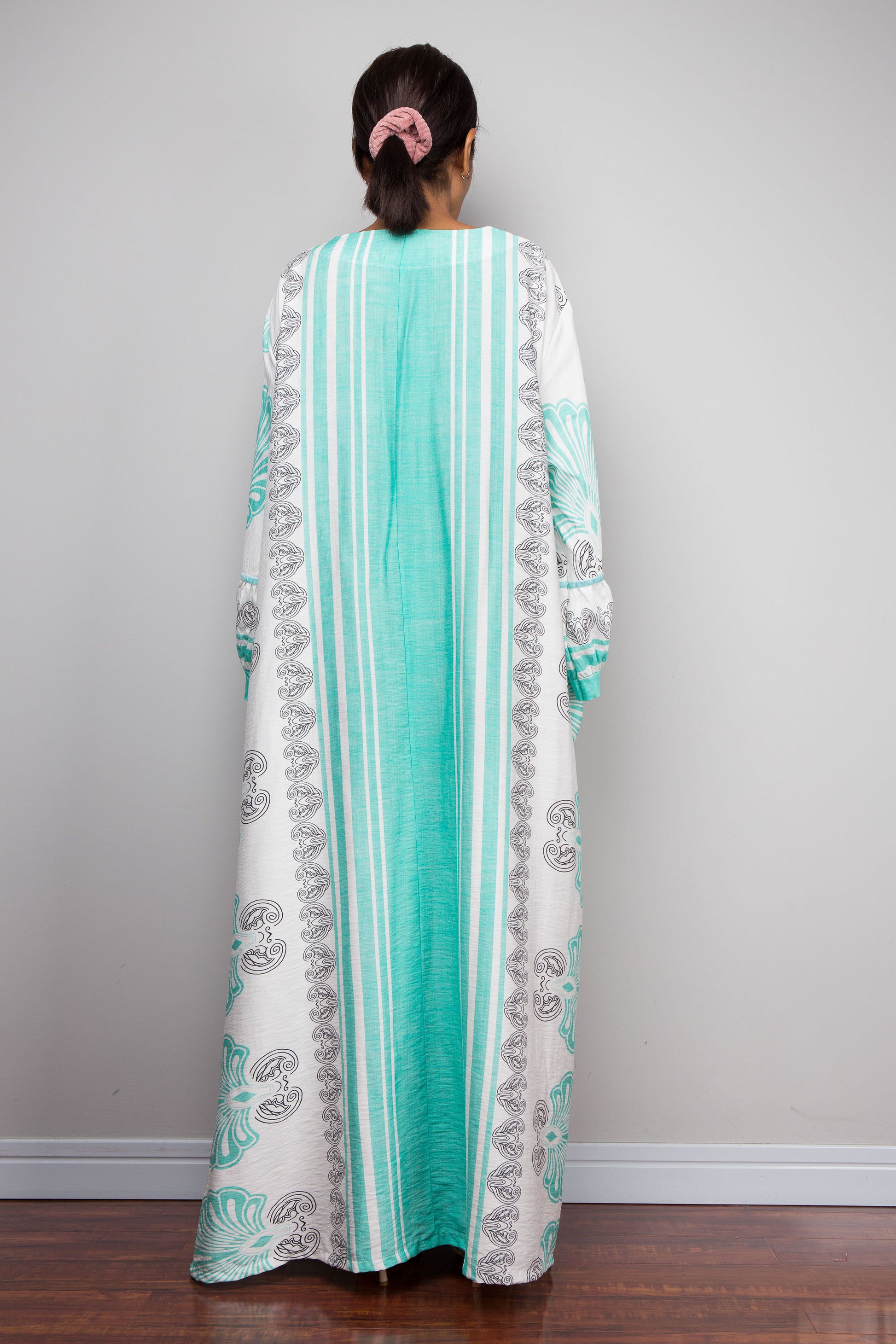 Full-length rear view shot of a model wearing the Nuichan bohemian caftan dress in mint green and white, highlighting the vertical-striped paneling, V-neckline,and functional side pockets.