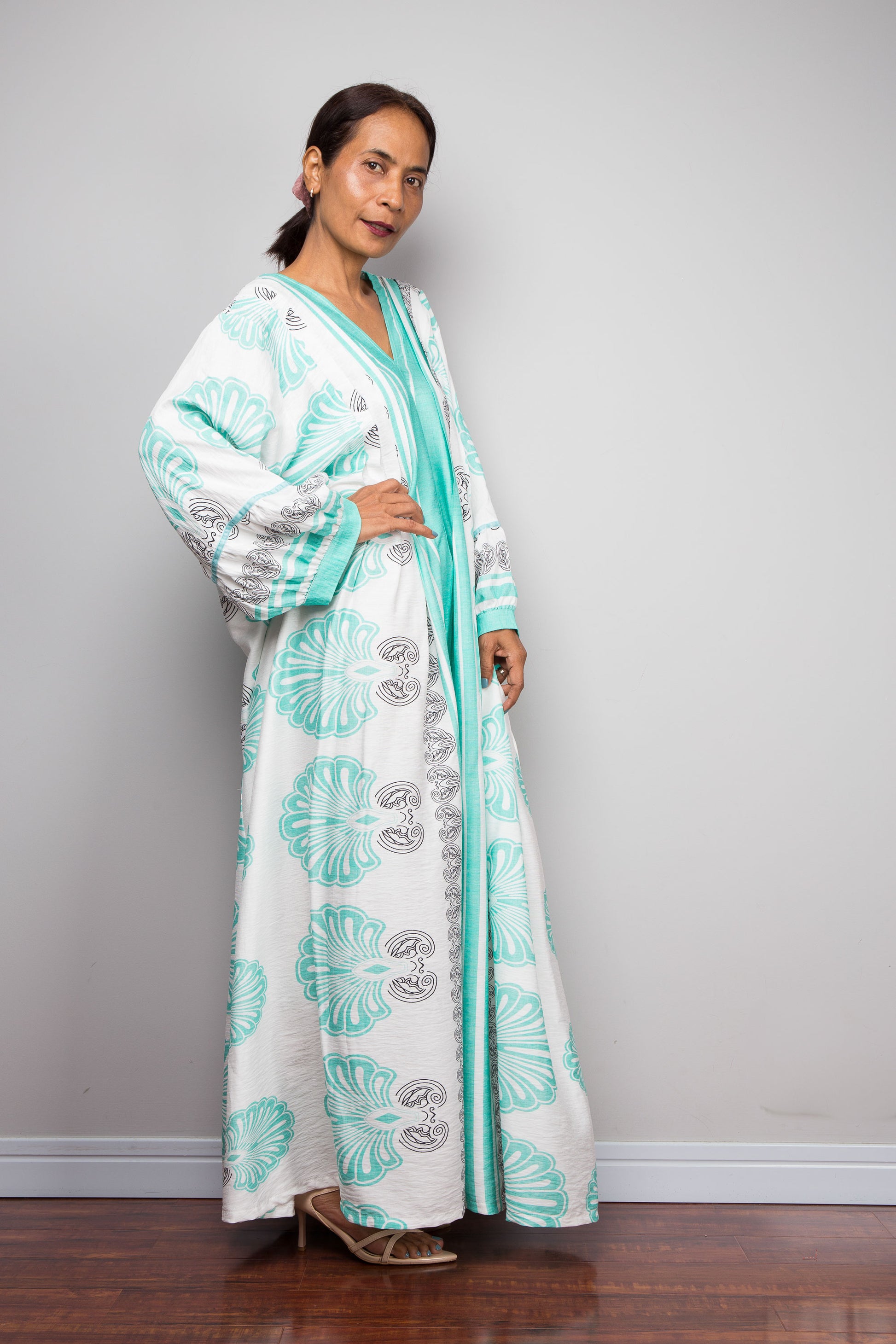 Side view of a petite female model wearing the Nuichan bohemian caftan dress in mint green and white, highlighting the vertical-striped paneling, V-neckline,and functional side pockets.