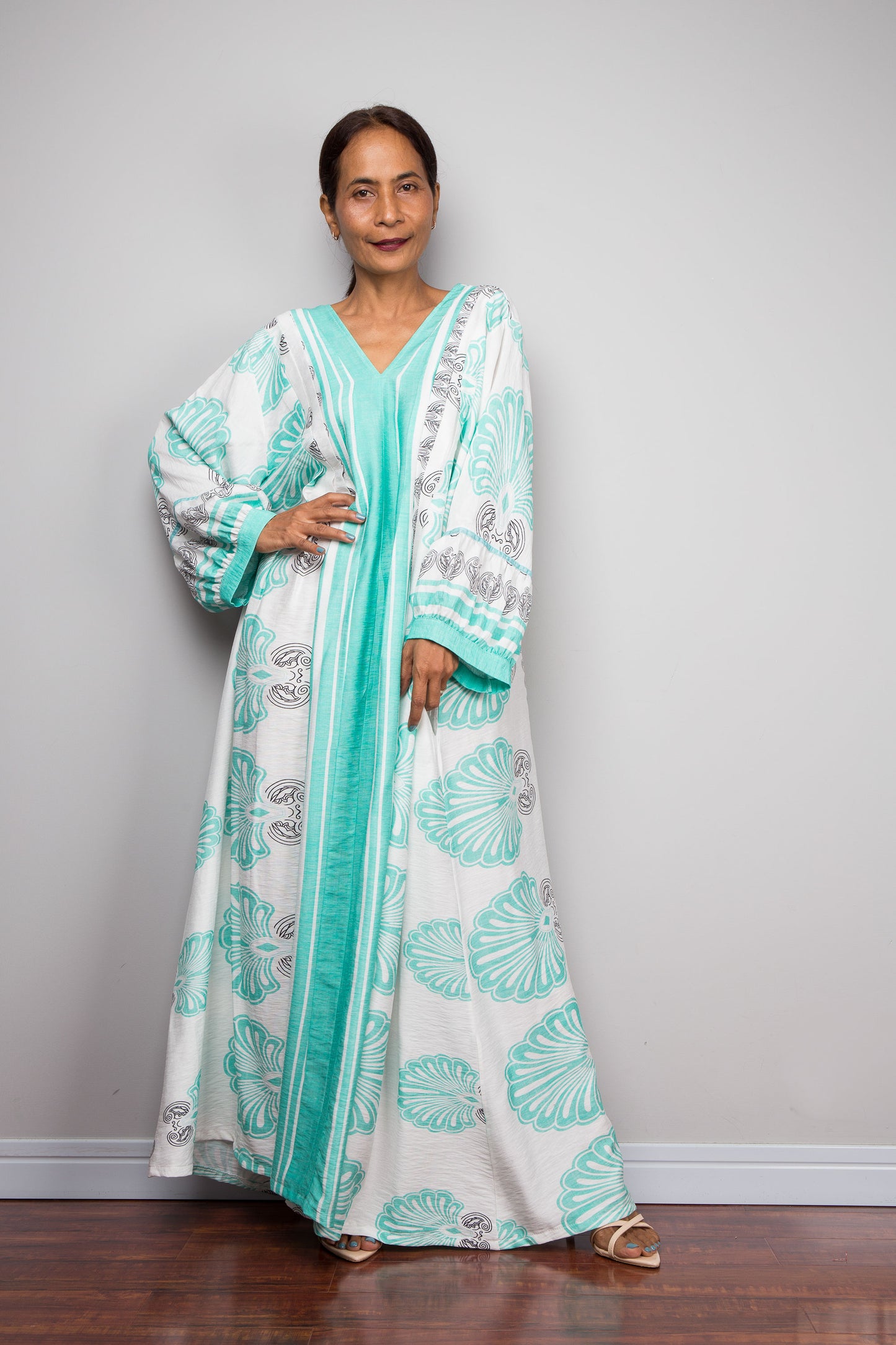 Photo of a female asian model wearing the Nuichan bohemian caftan dress in mint green and white, highlighting the vertical-striped paneling, V-neckline,and functional side pockets.