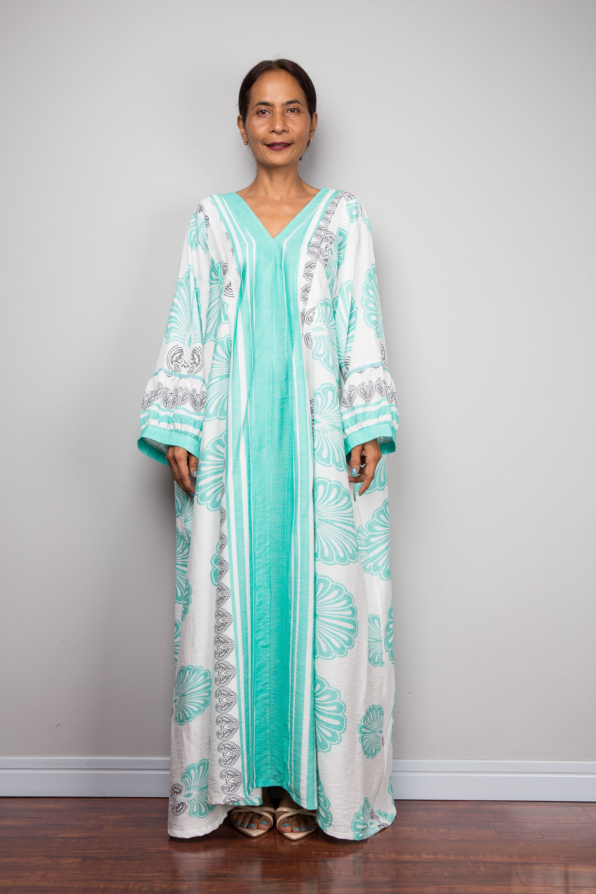 Front facing shot of a model wearing the Nuichan bohemian caftan dress in mint green and white, highlighting the vertical-striped paneling, V-neckline,and functional side pockets.