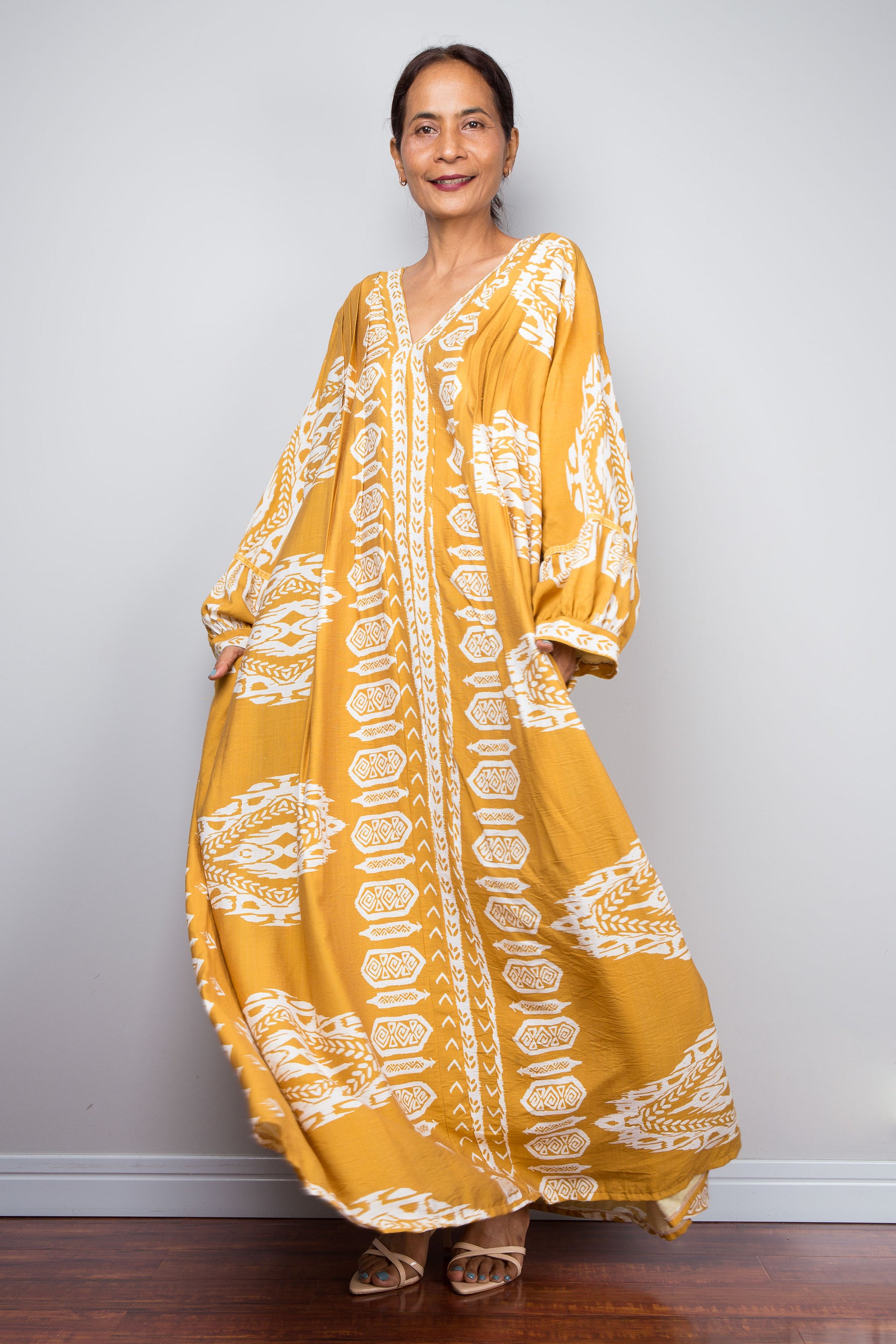 Front-facing studio shot of a model in the Nuichan mustard yellow bohemian caftan dress with hands in the pockets, highlighting the voluminous bishop sleeves with gathered cuffs and bold white tribal print.