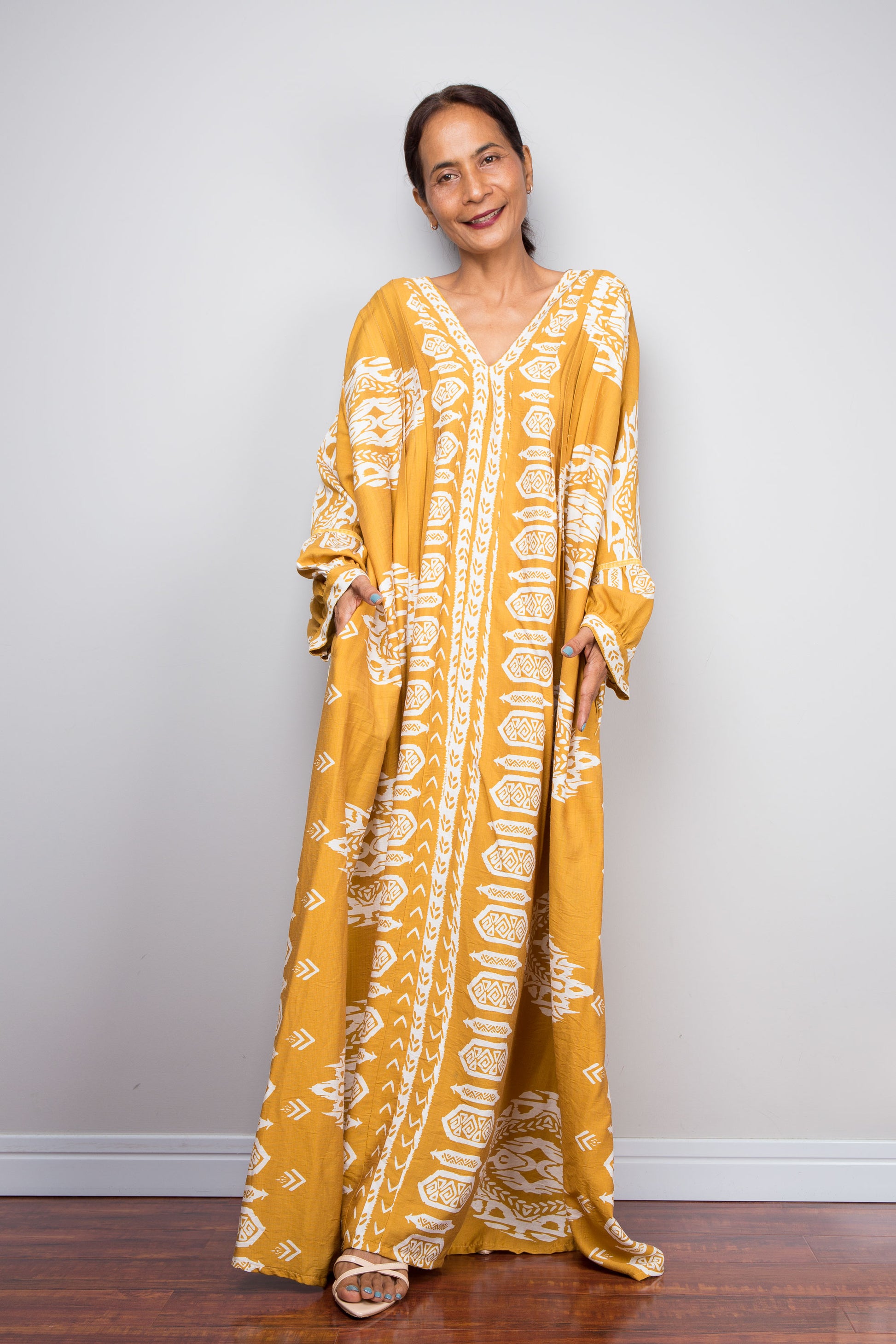 Full-length front view of a model wearing the Nuichan bohemian kaftan maxi dress in mustard yellow and white, showcasing the flowing A-line silhouette, tribal ikat print, and deep V-neckline.