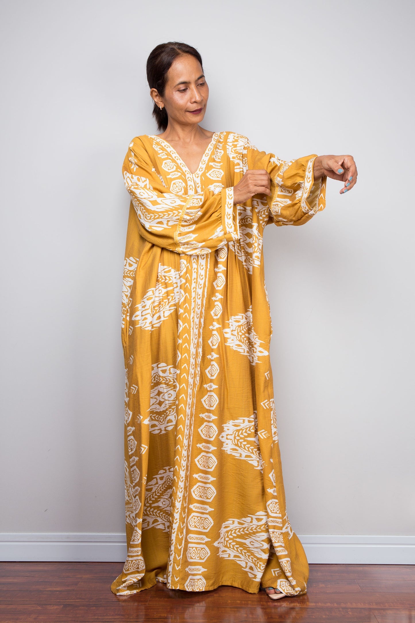 Full-length view of a model wearing the Nuichan bohemian kaftan maxi dress in mustard yellow and white, showcasing the bishop sleeves, tribal ikat print, and deep V-neckline.