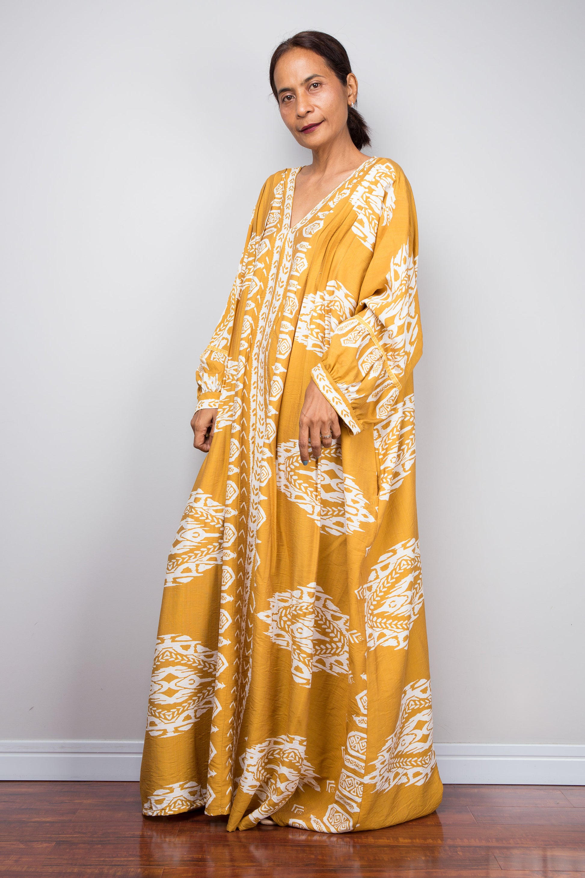 Side profile view of a female model wearing the Nuichan mustard and white ikat kaftan dress, emphasising the dramatic floor-length sweep, gathered sleeve cuffs, and intricate placement border print.