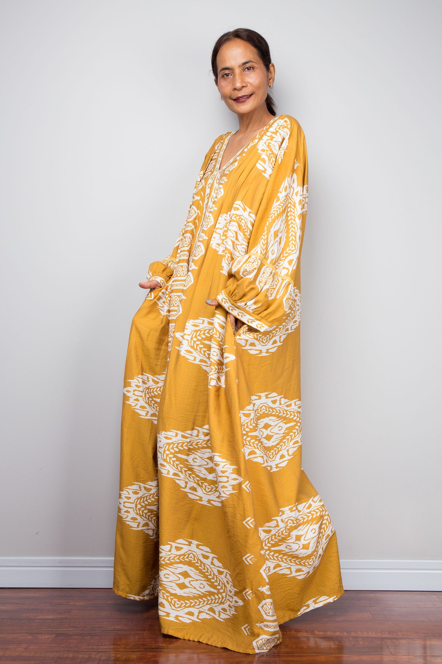 Side view shot of a model in the Nuichan mustard yellow bohemian caftan dress with hands in pockets, highlighting the voluminous bishop sleeves with gathered cuffs and bold white tribal print.