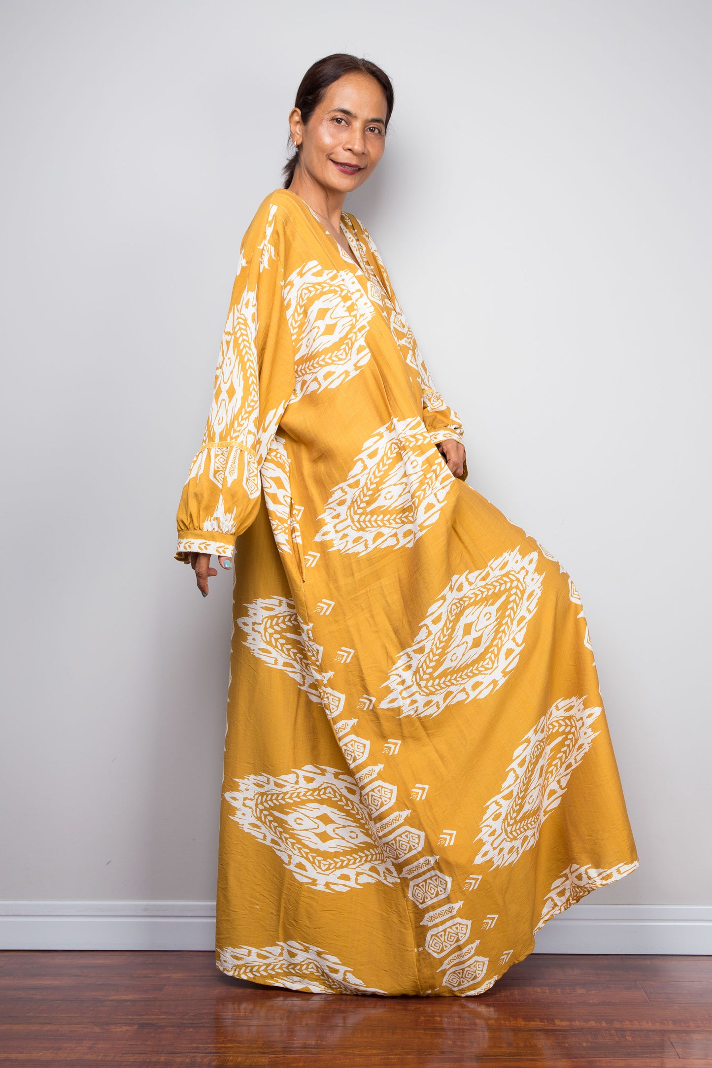 Side profile view of a model wearing the Nuichan mustard and white ikat kaftan dress, emphasising the dramatic floor-length sweep, gathered sleeve cuffs, and intricate placement border print.