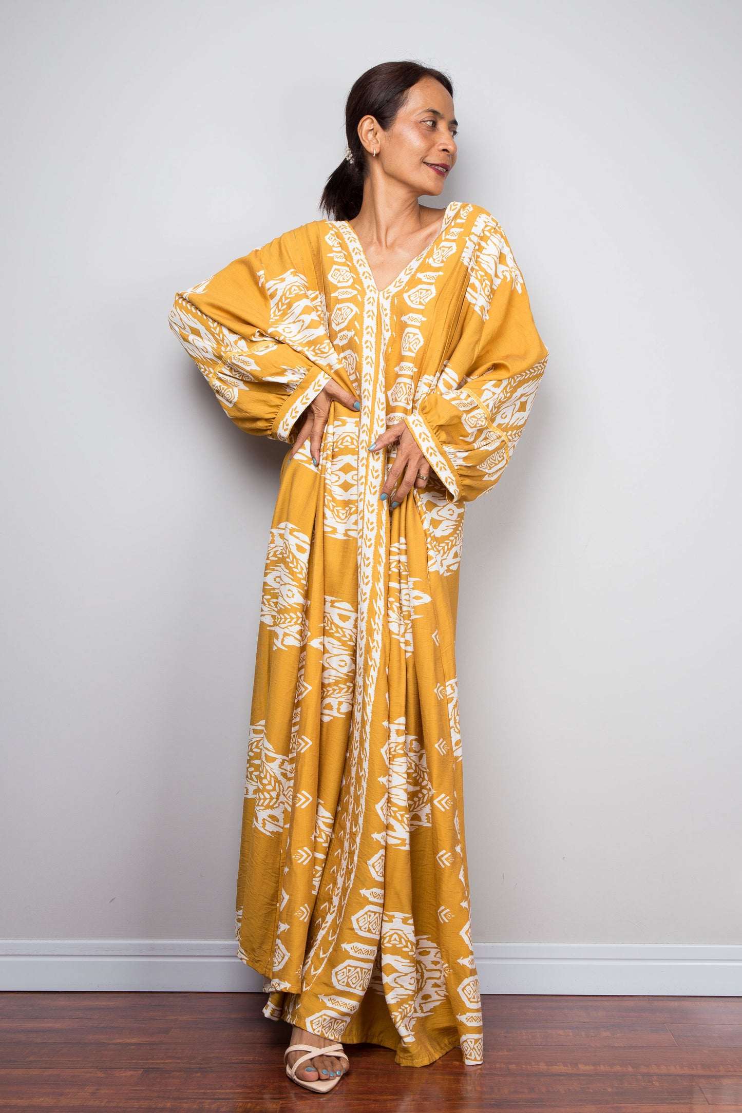 Front-facing studio shot of a model in the Nuichan mustard yellow bohemian caftan dress with hands on hips, highlighting the voluminous bishop sleeves with gathered cuffs and white tribal print.