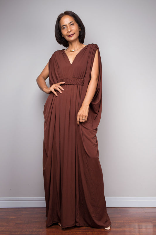 Woman wearing a brown flowing caftan dress by Nuichan against a plain background