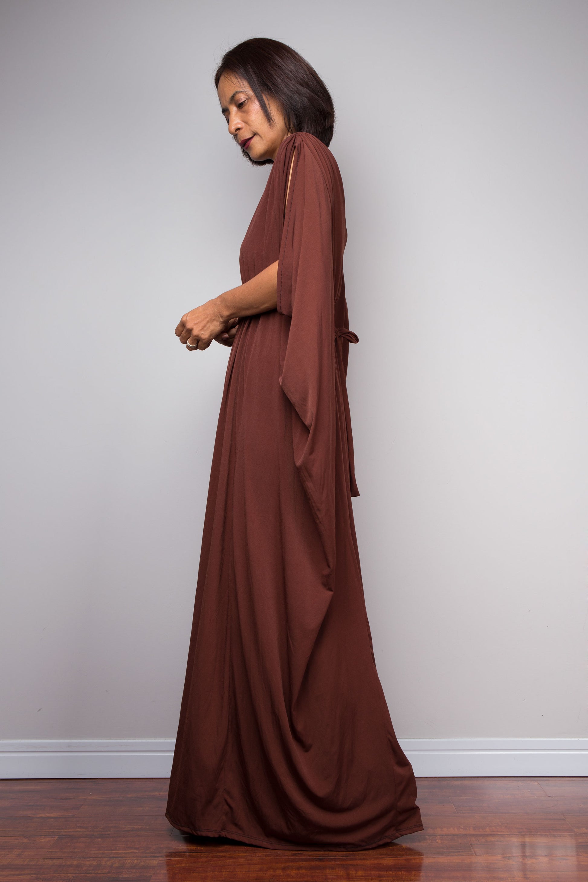 Woman wearing a long brown caftan dress against a plain background