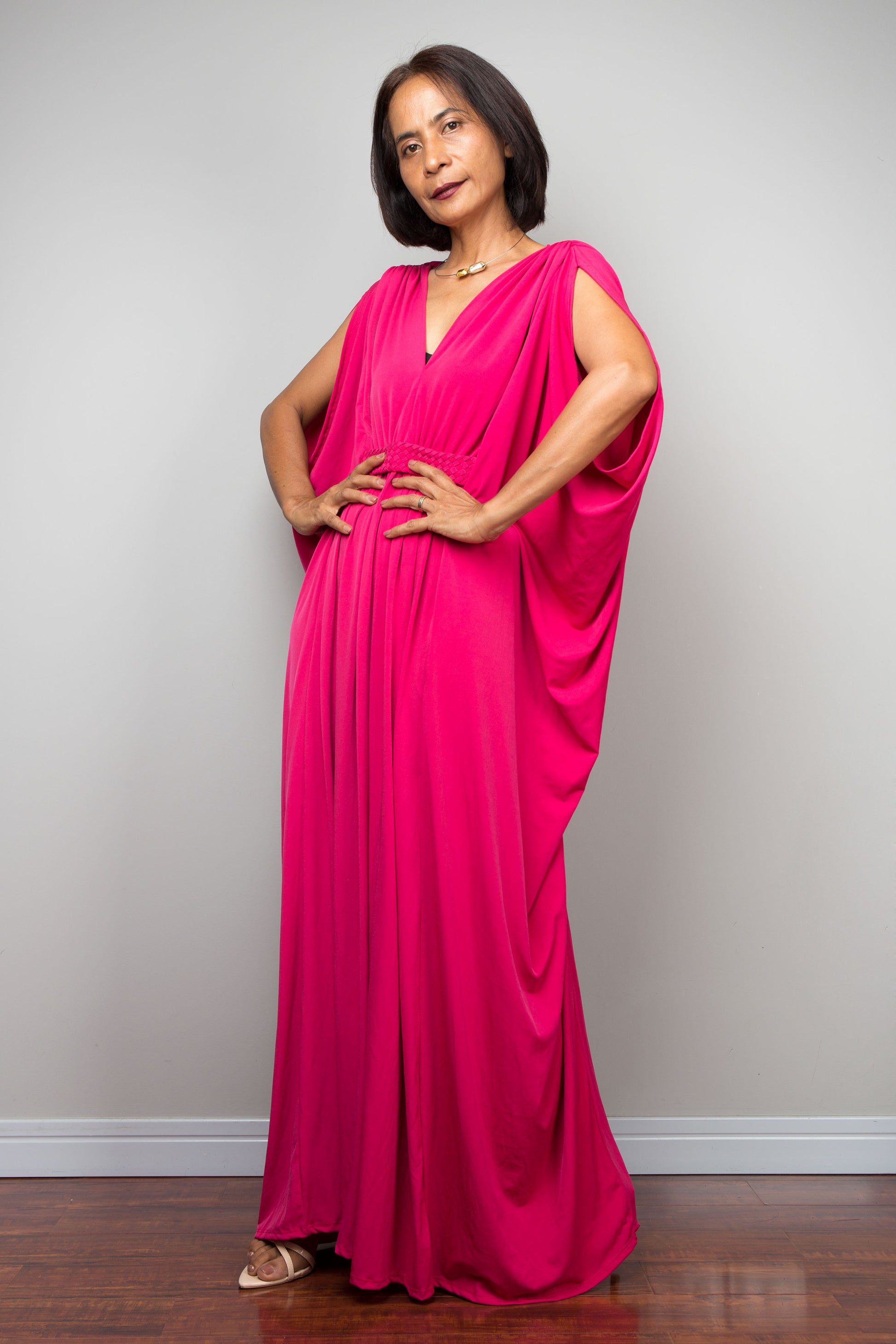 Petite woman wearing a bright pink kaftan maxi dress against a plain background