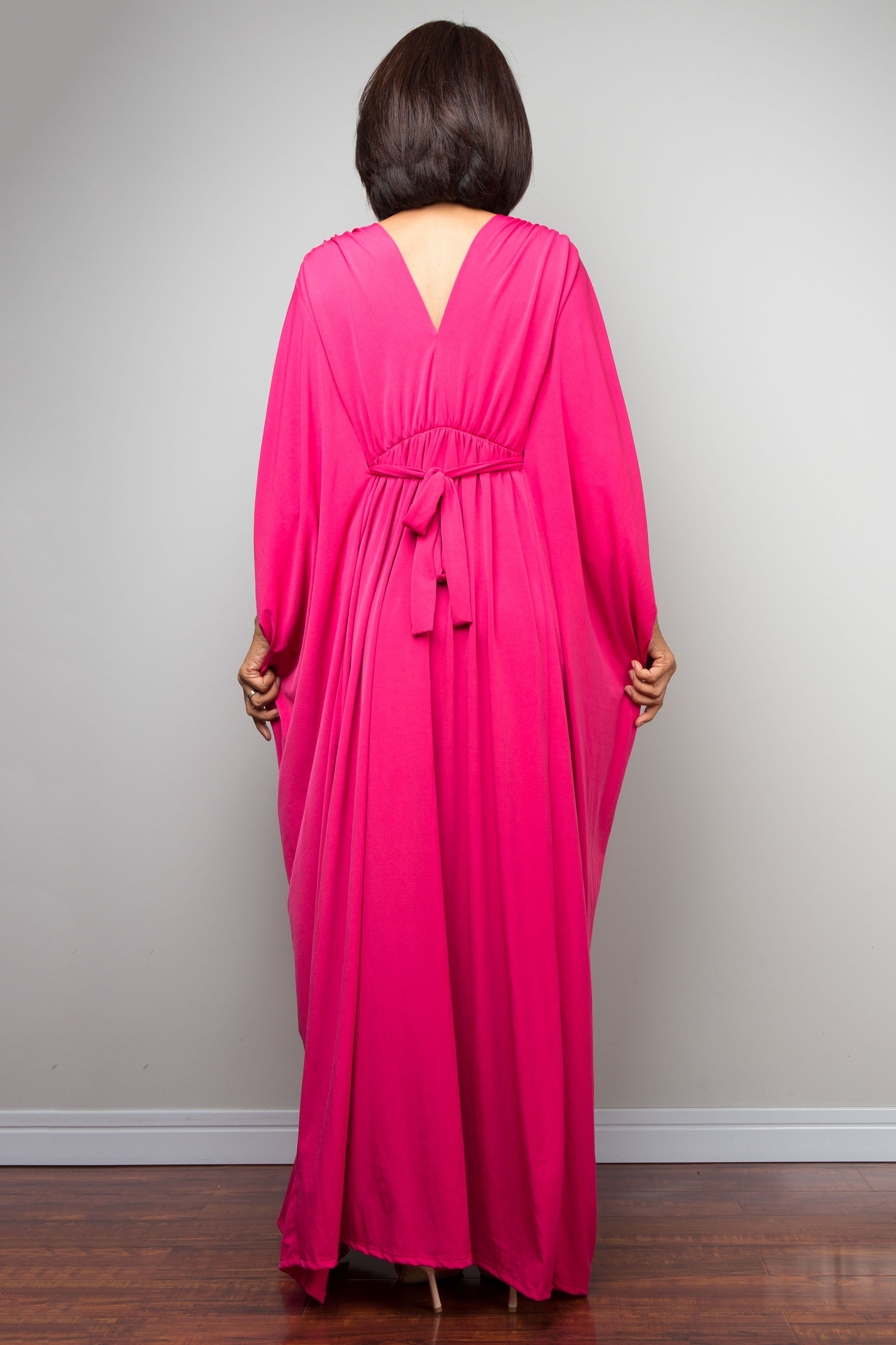 Petite woman wearing a bright pink caftan dress with a deep neckline and long sleeves against a plain background.