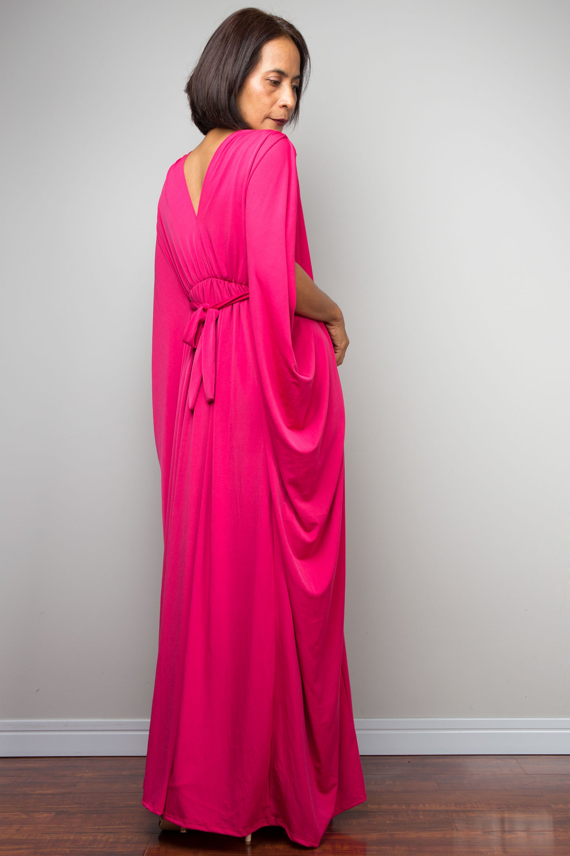 Petite woman wearing a hot pink caftan maxi dress against a plain background