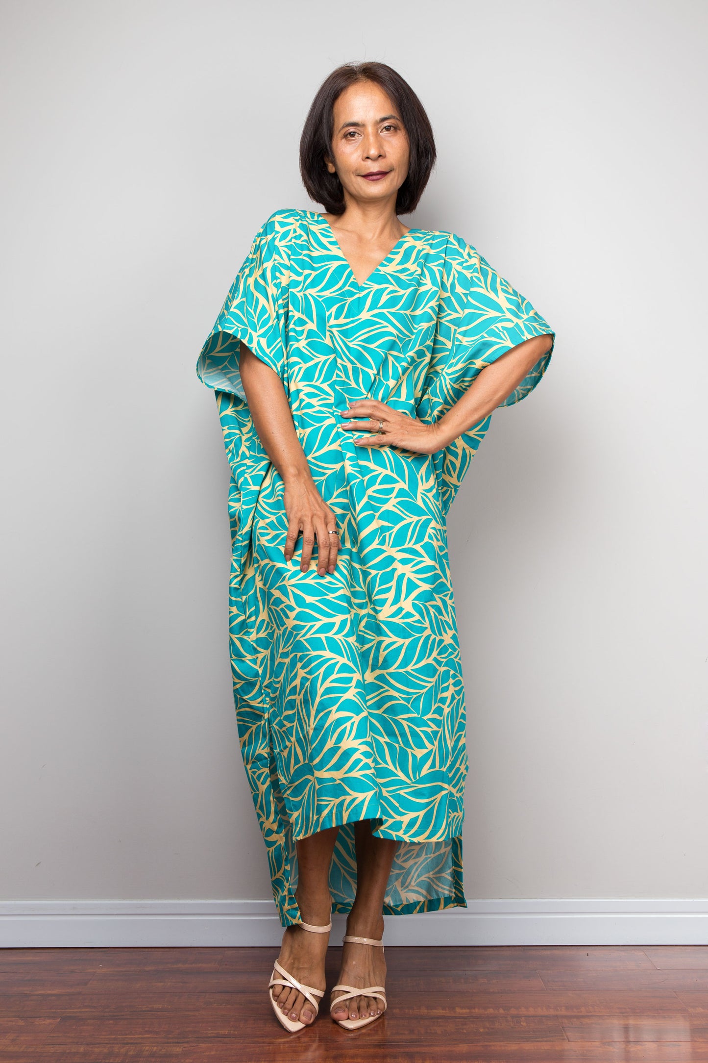 Woman wearing a teal and yellow patterned caftan dress for petite against a plain background