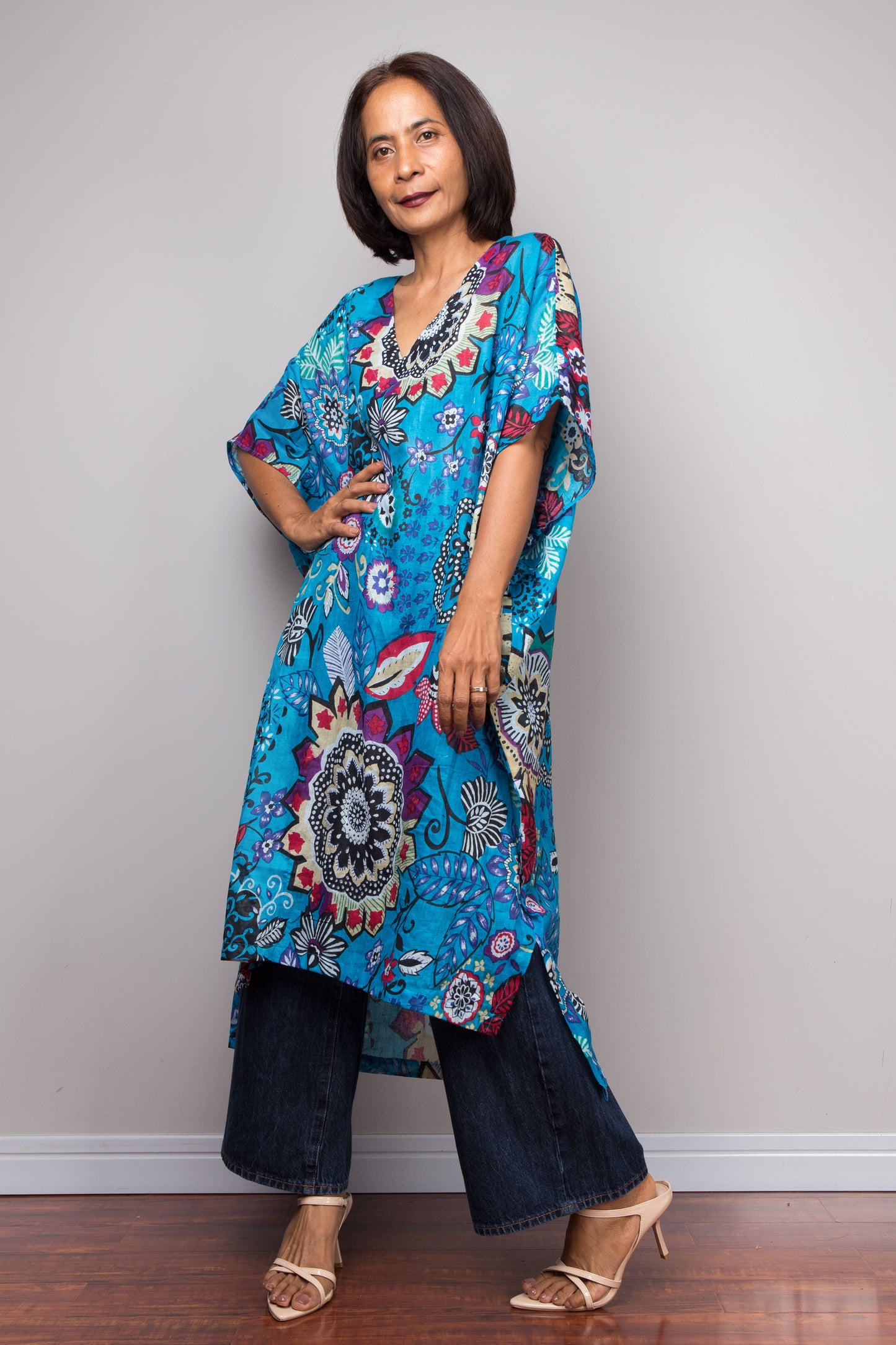 Woman wearing a colorful floral caftan dress against a plain background