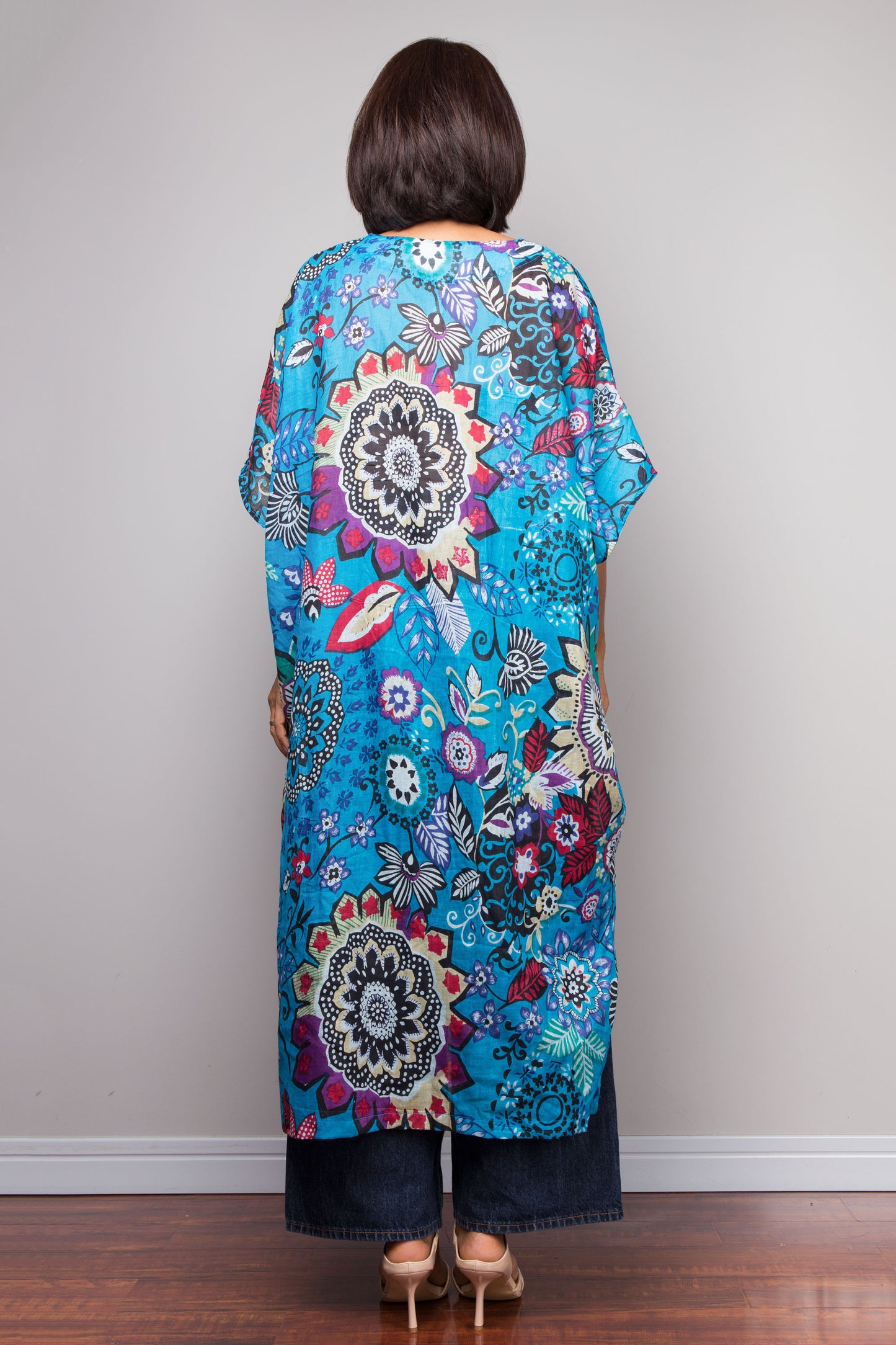 Woman wearing a colorful floral and mandala patterned dress against a plain background