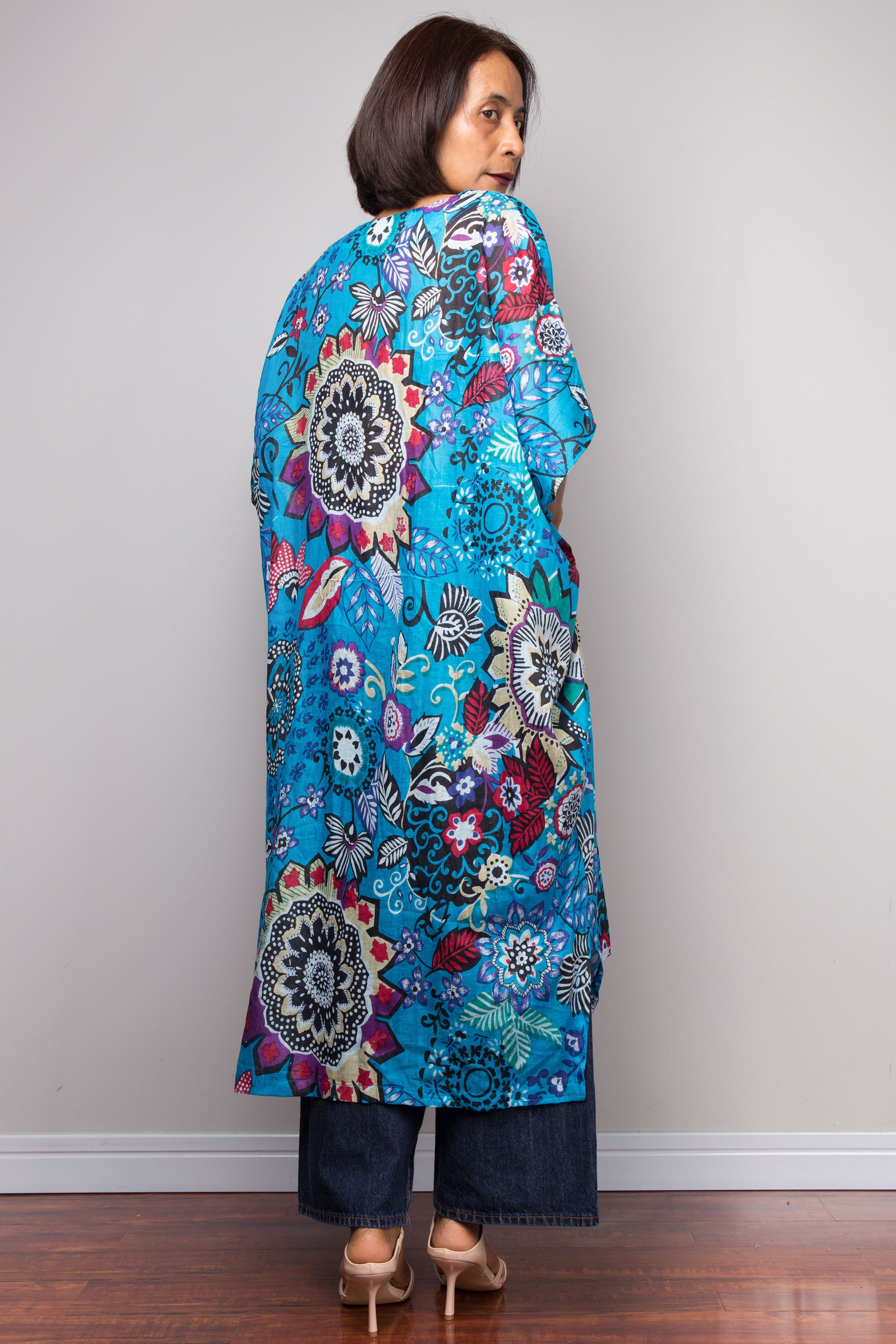 Woman wearing a colorful floral caftan against a plain background