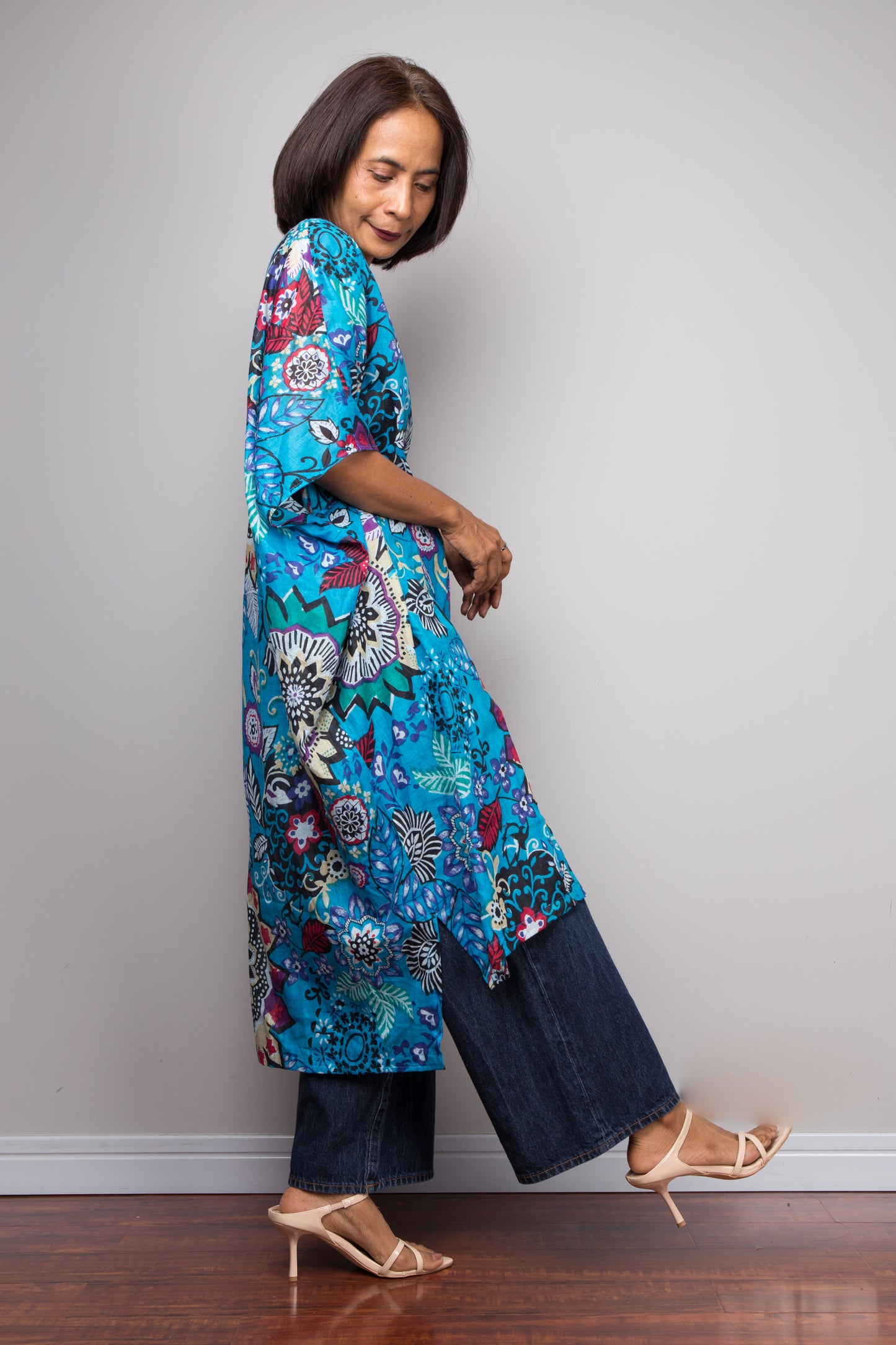 Woman wearing a colorful floral caftan dress with dark pants against a plain background