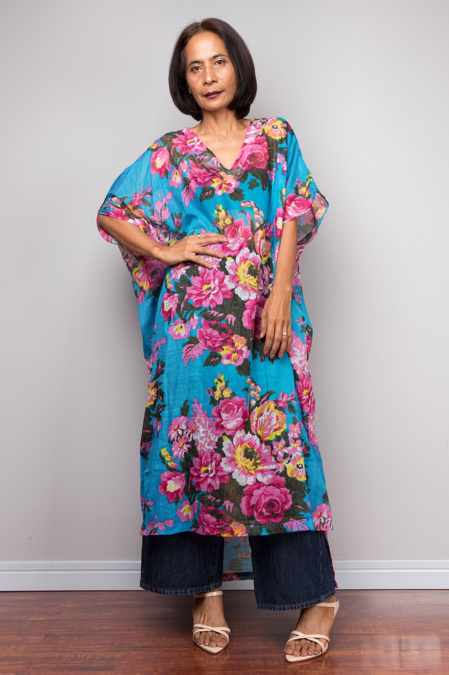 Woman wearing a colourful floral caftan dress against a plain background