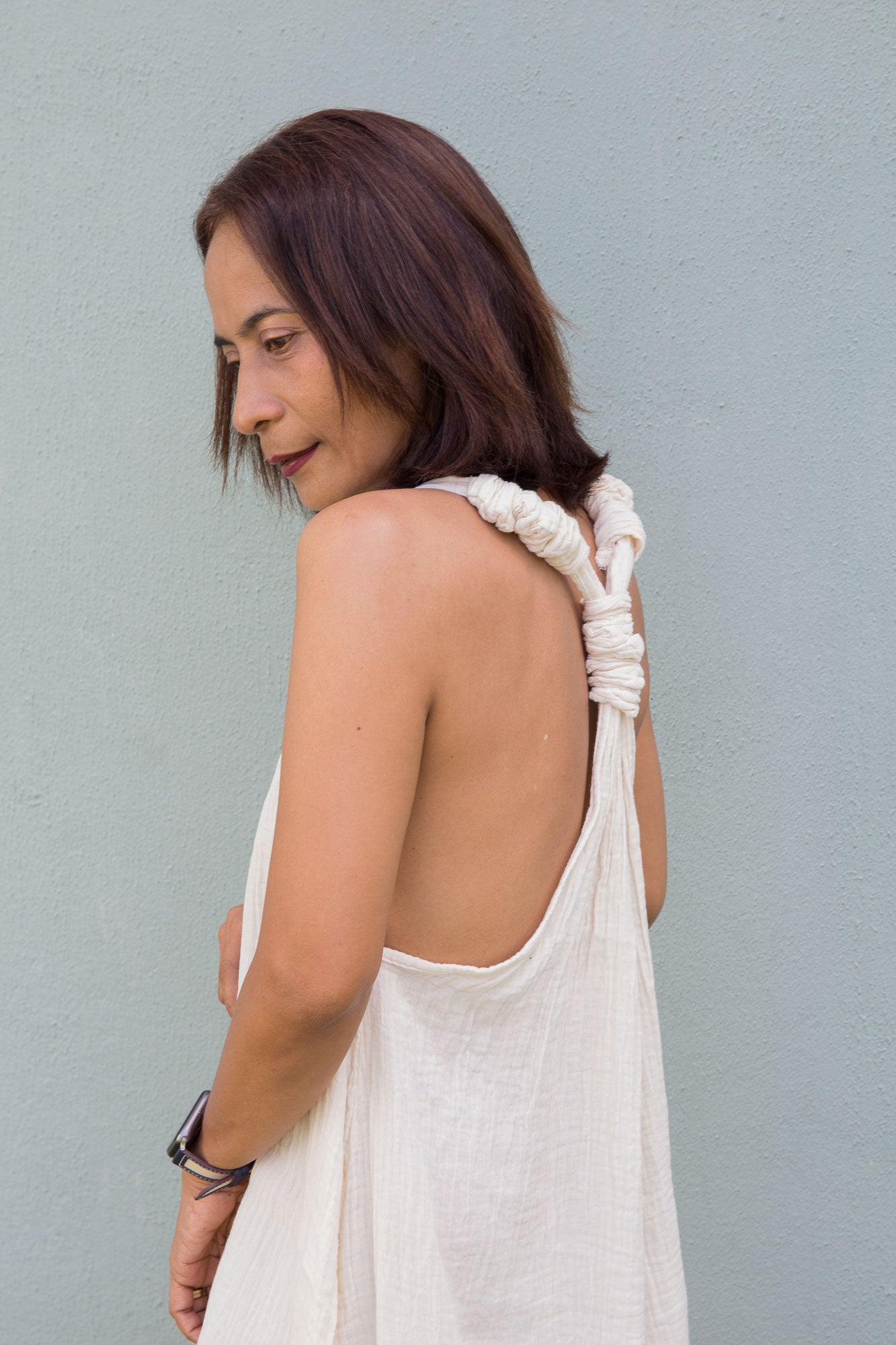 Woman wearing a white sleeveless cotton gauze dress against a gray background