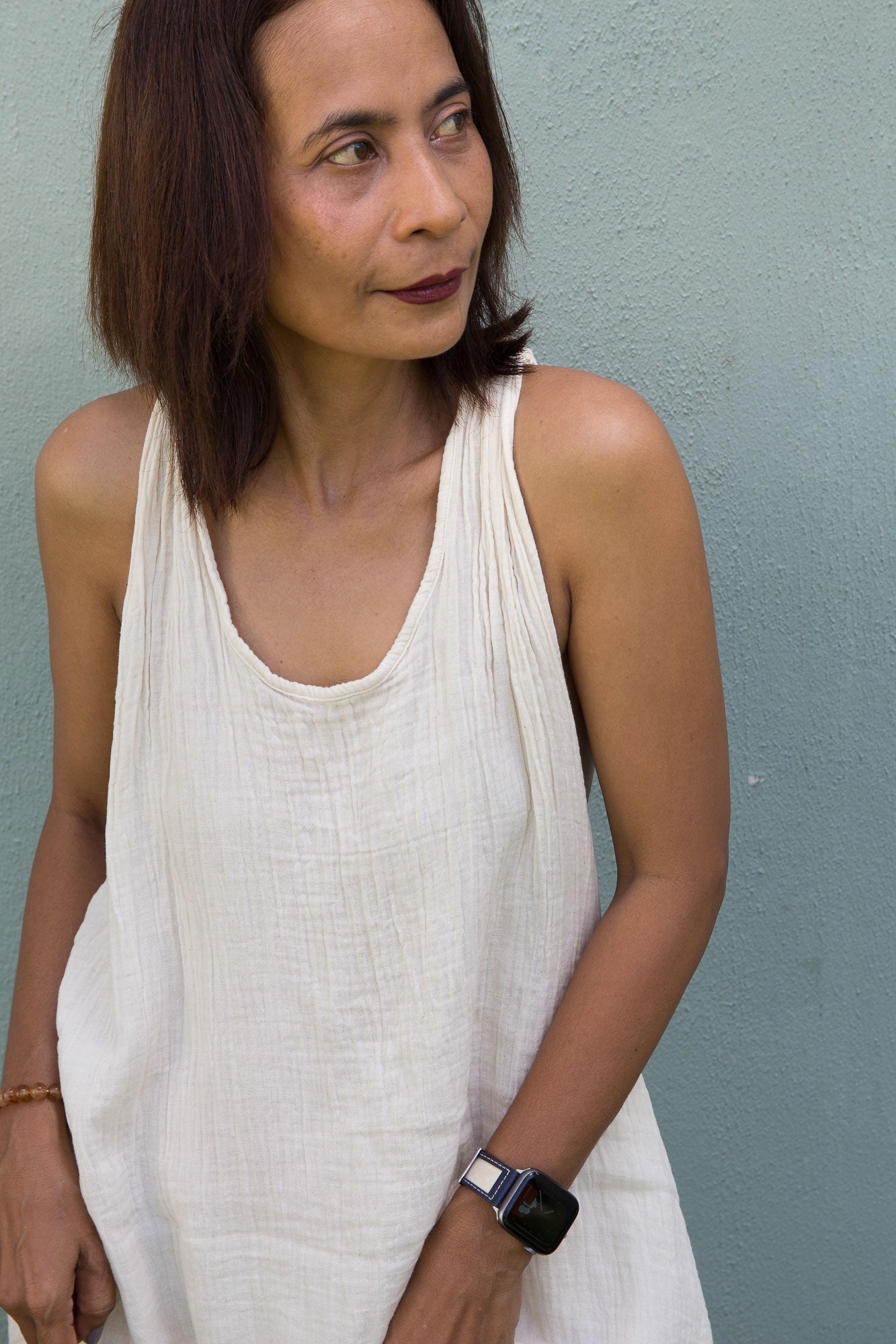 Woman wearing a white sleeveless cotton gauze halter dress against a light blue wall