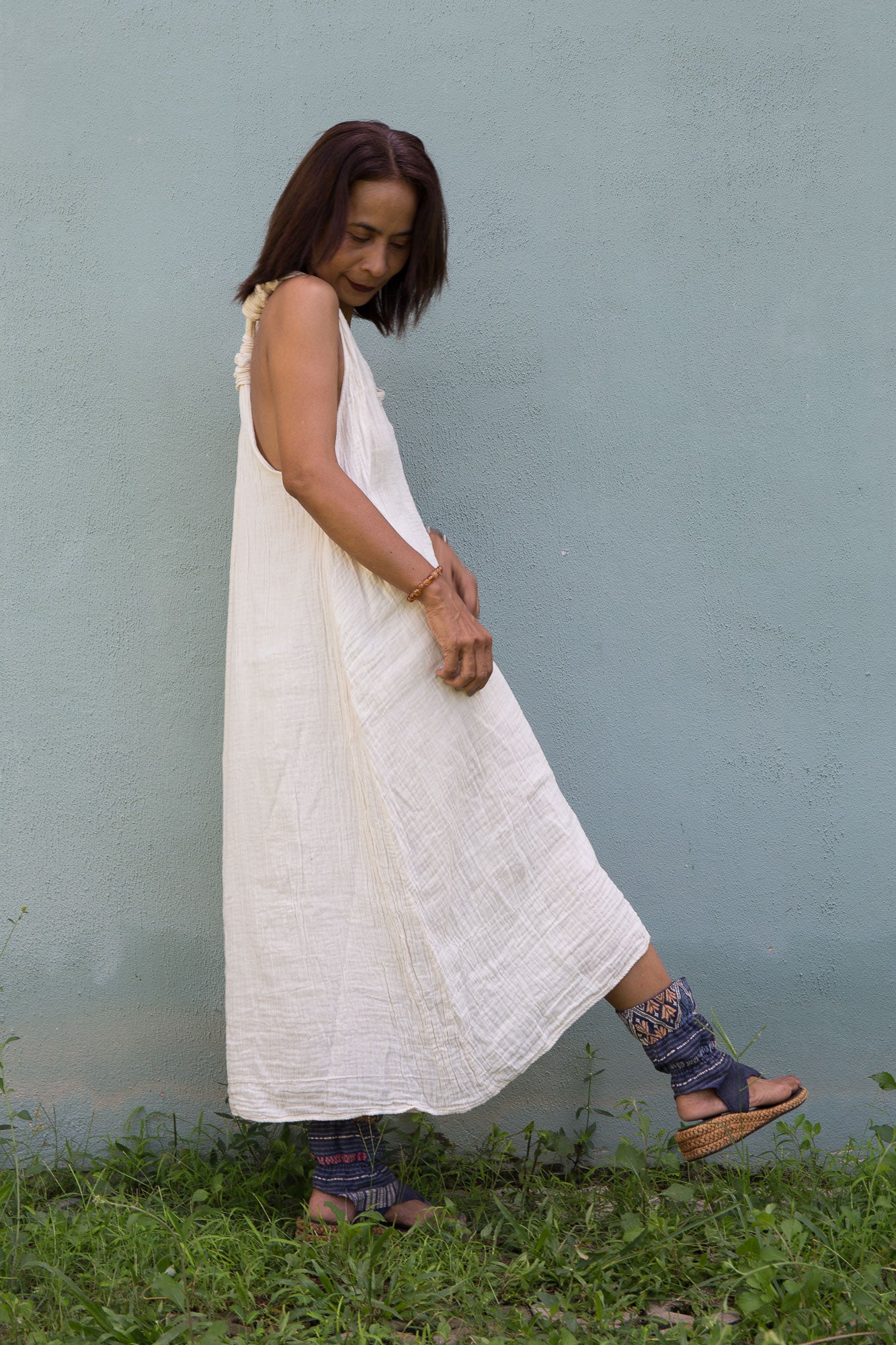 Woman in a white cotton dress standing in grass against a light blue wall