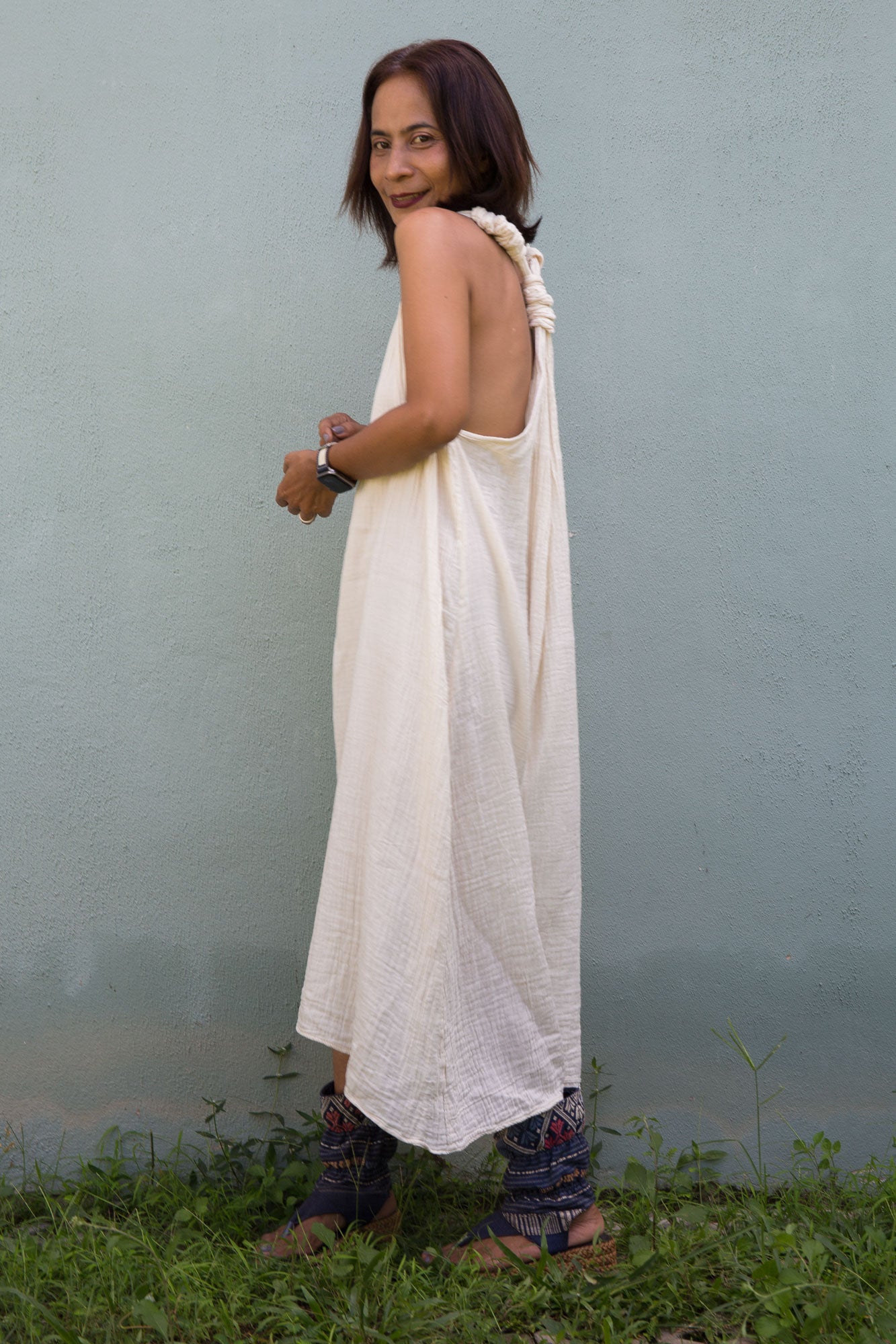Woman wearing a white dress standing in grass against a plain background