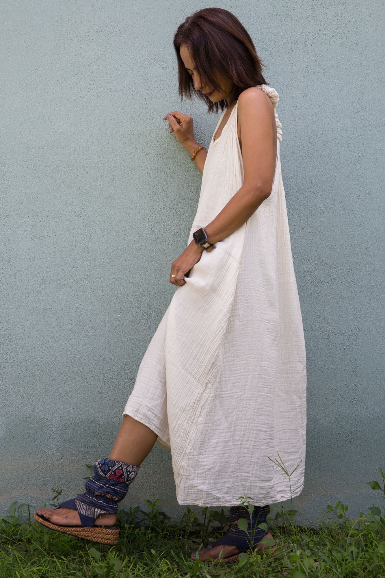 Woman wearing a white sleeveless cotton gauze dress against a light blue wall.