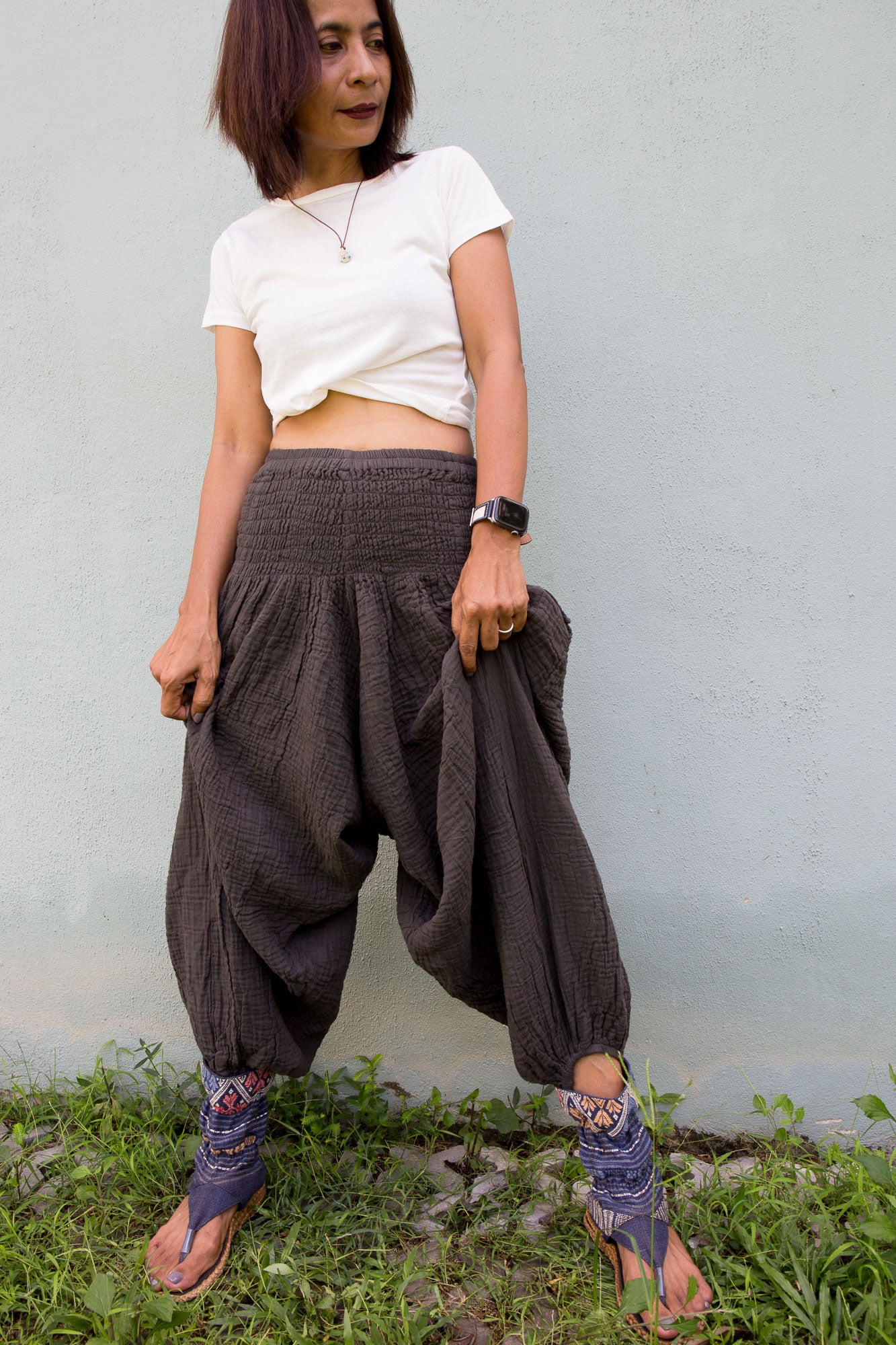 Person wearing a white top and gray harem pants standing against a light gray wall.