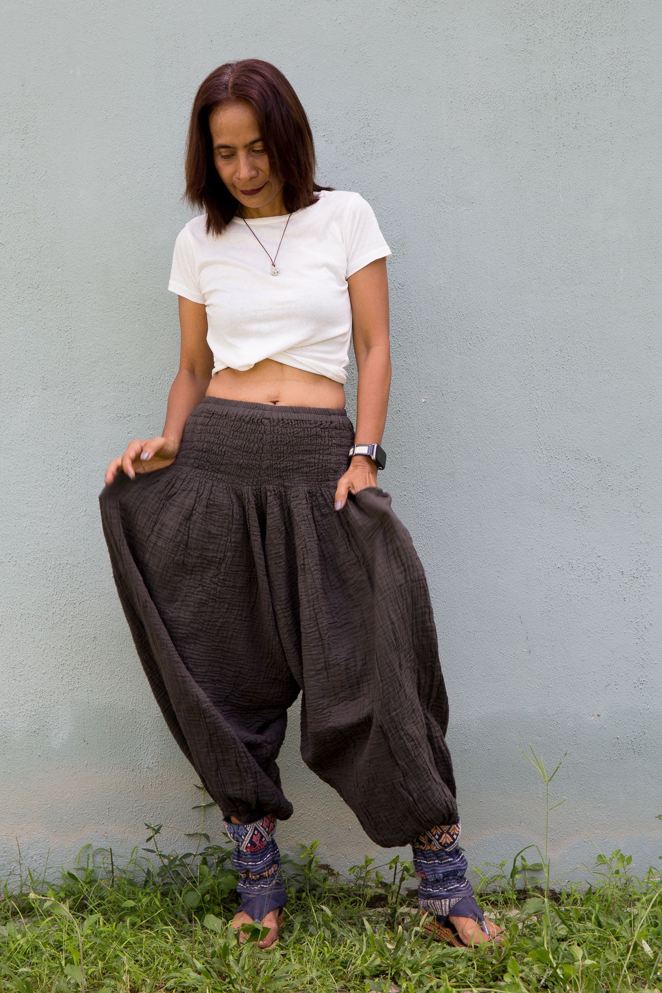 Woman wearing a white top and charcoal grey wide-leg cotton harem pants standing against a plain background