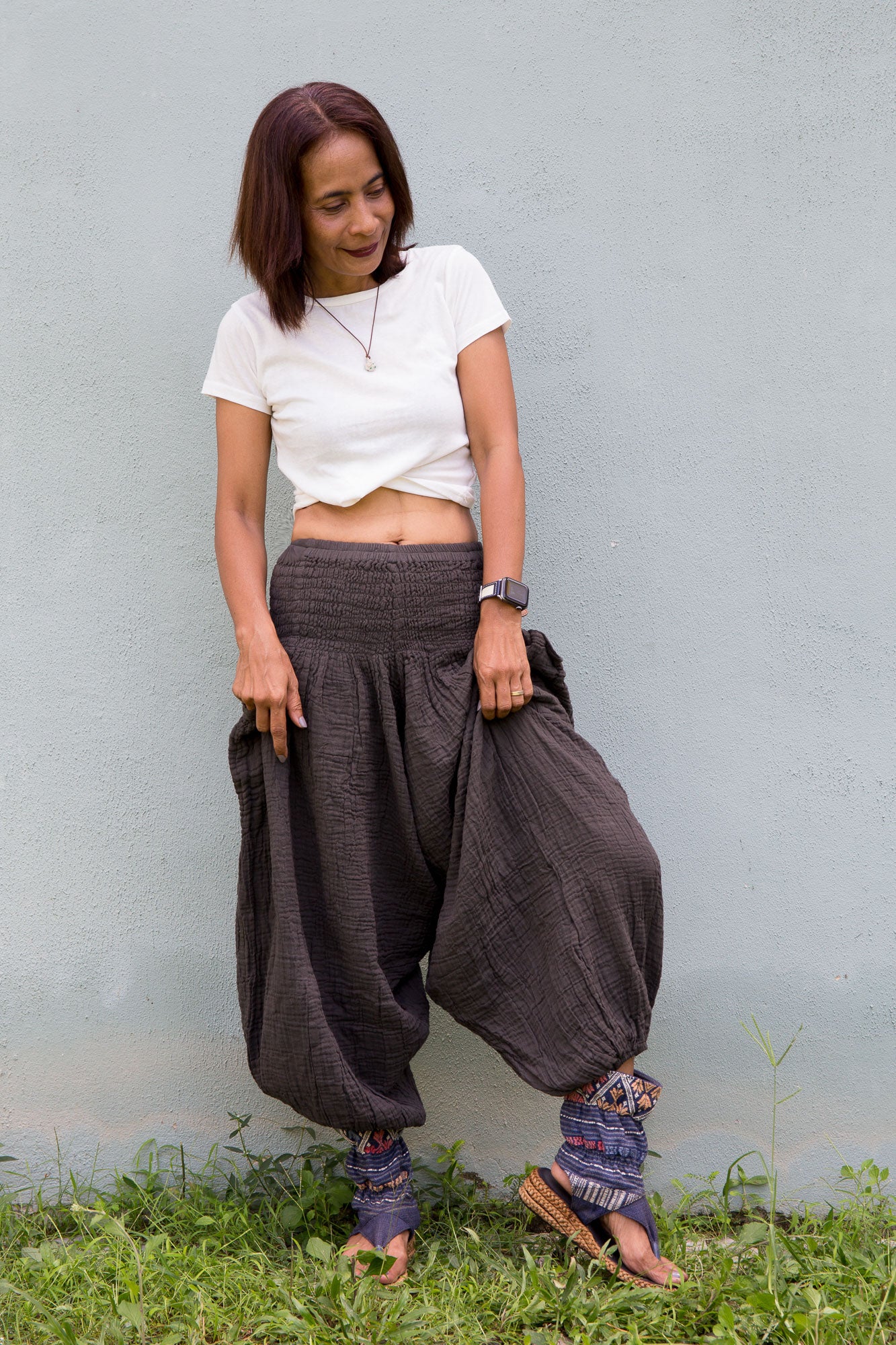 Woman wearing a white top and grey wide-leg pants standing against a light blue wall.