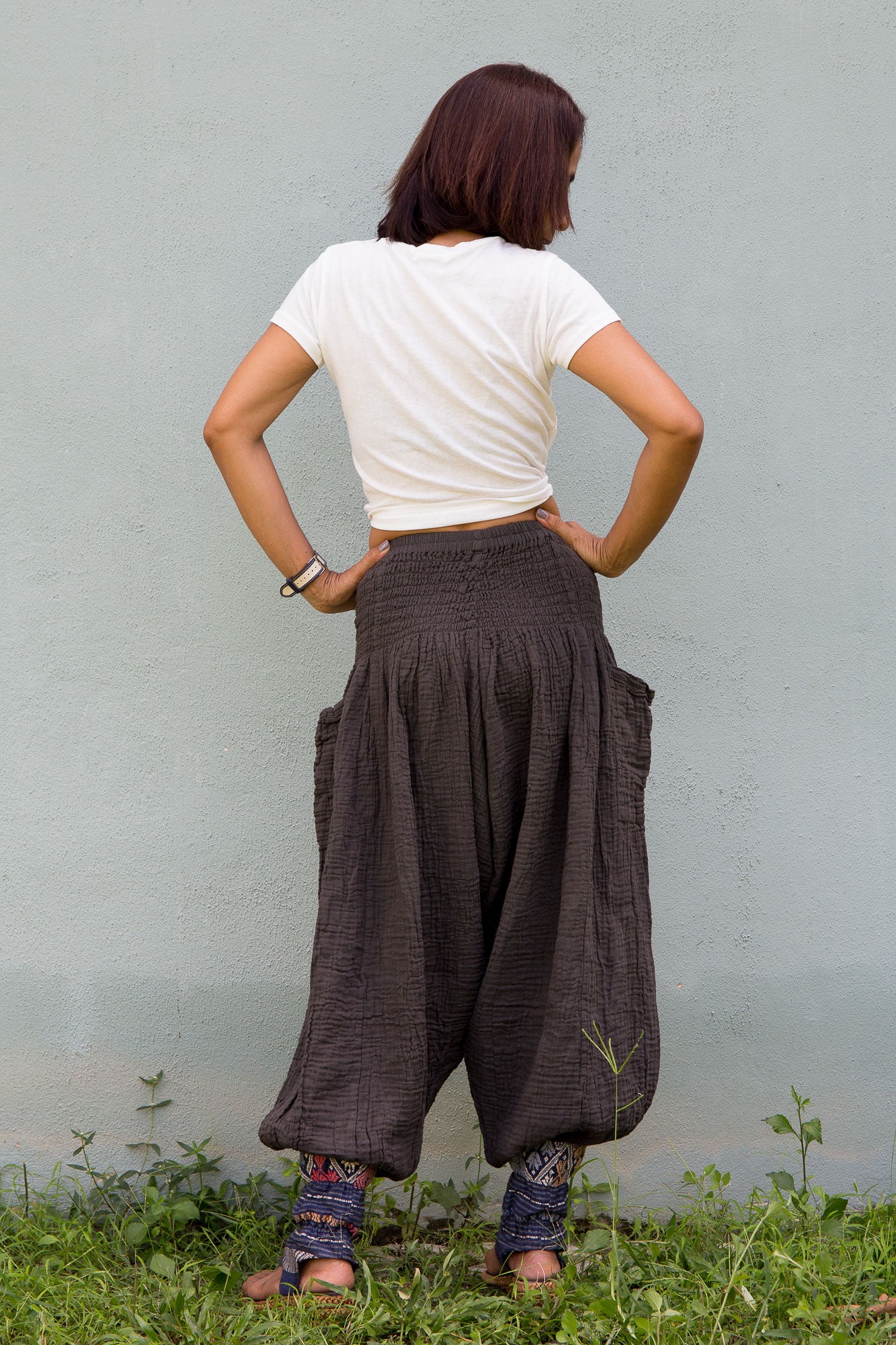 Person wearing grey wide-leg pants with pockets and a white top, standing in grass with a plain background