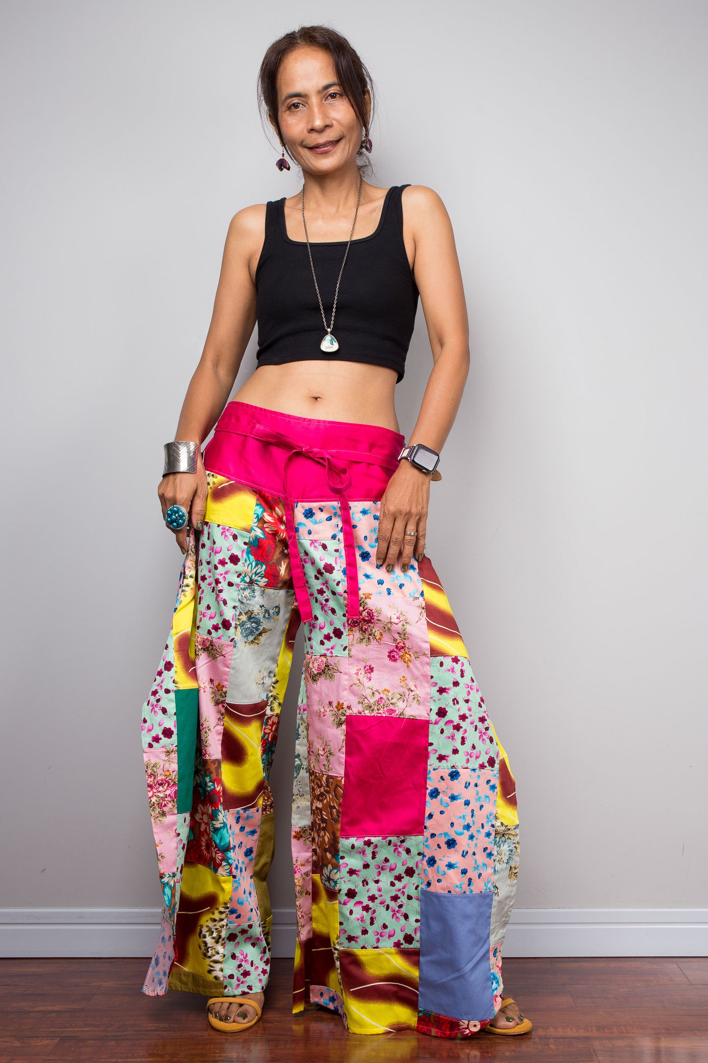 Petite model wearing the Nuichan pastel patchwork wide leg palazzo pants, showcasing the vivid pink self-tie sash waistband, full ultra-wide leg silhouette, and hand-sewn quilt-style patchwork construction in mixed cotton satin pastel prints including mint, blush pink, teal, yellow satin and floral panels, styled with a black crop top