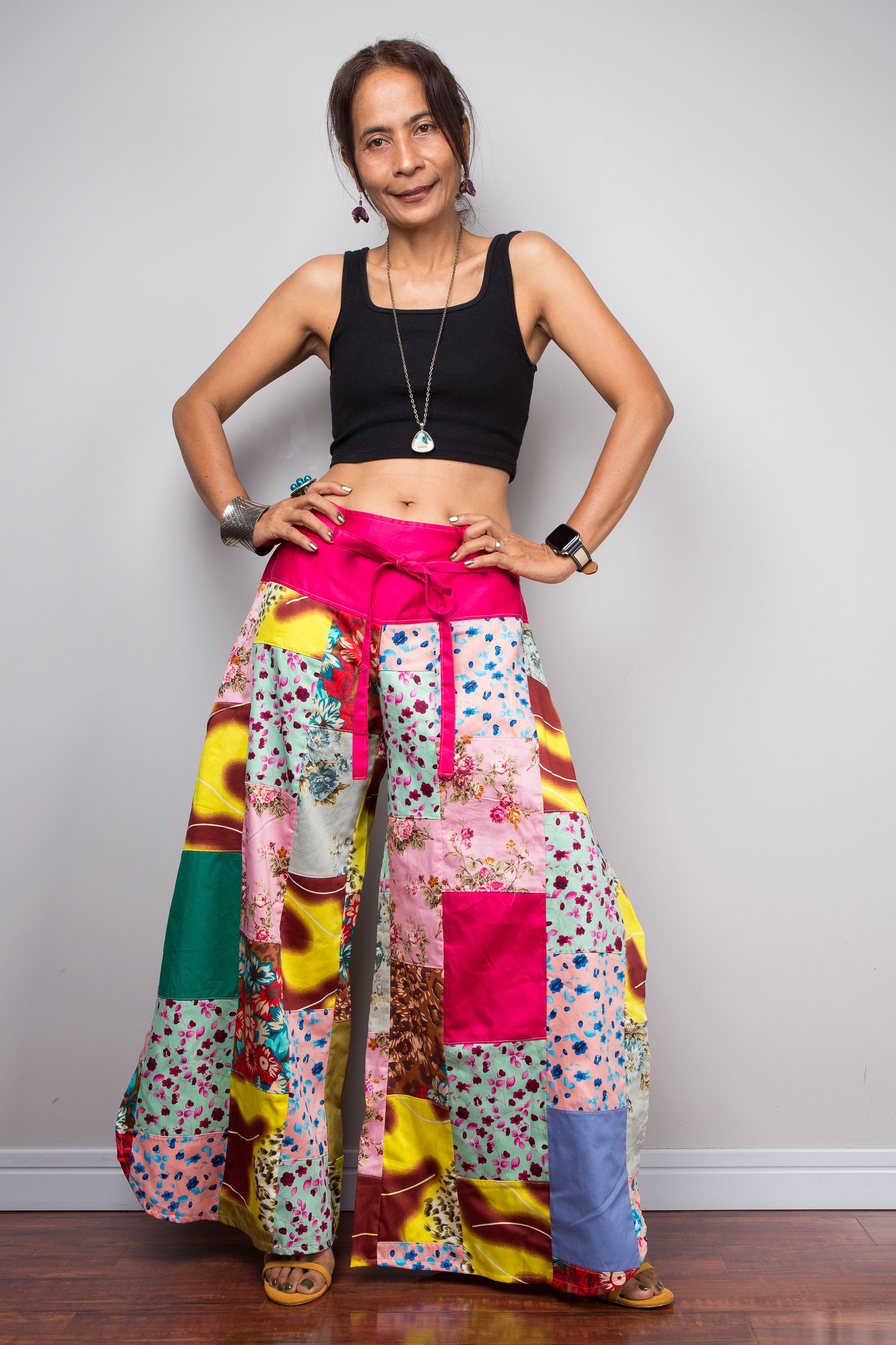 Front view of a model wearing the Nuichan pastel patchwork wide leg palazzo pants, showcasing the hot pink self-tie sash waistband, full ultra-wide leg silhouette, and hand-sewn quilt-style patchwork construction in mixed cotton satin pastel prints including mint, blush pink, teal, yellow satin and floral panels, styled with a black crop top