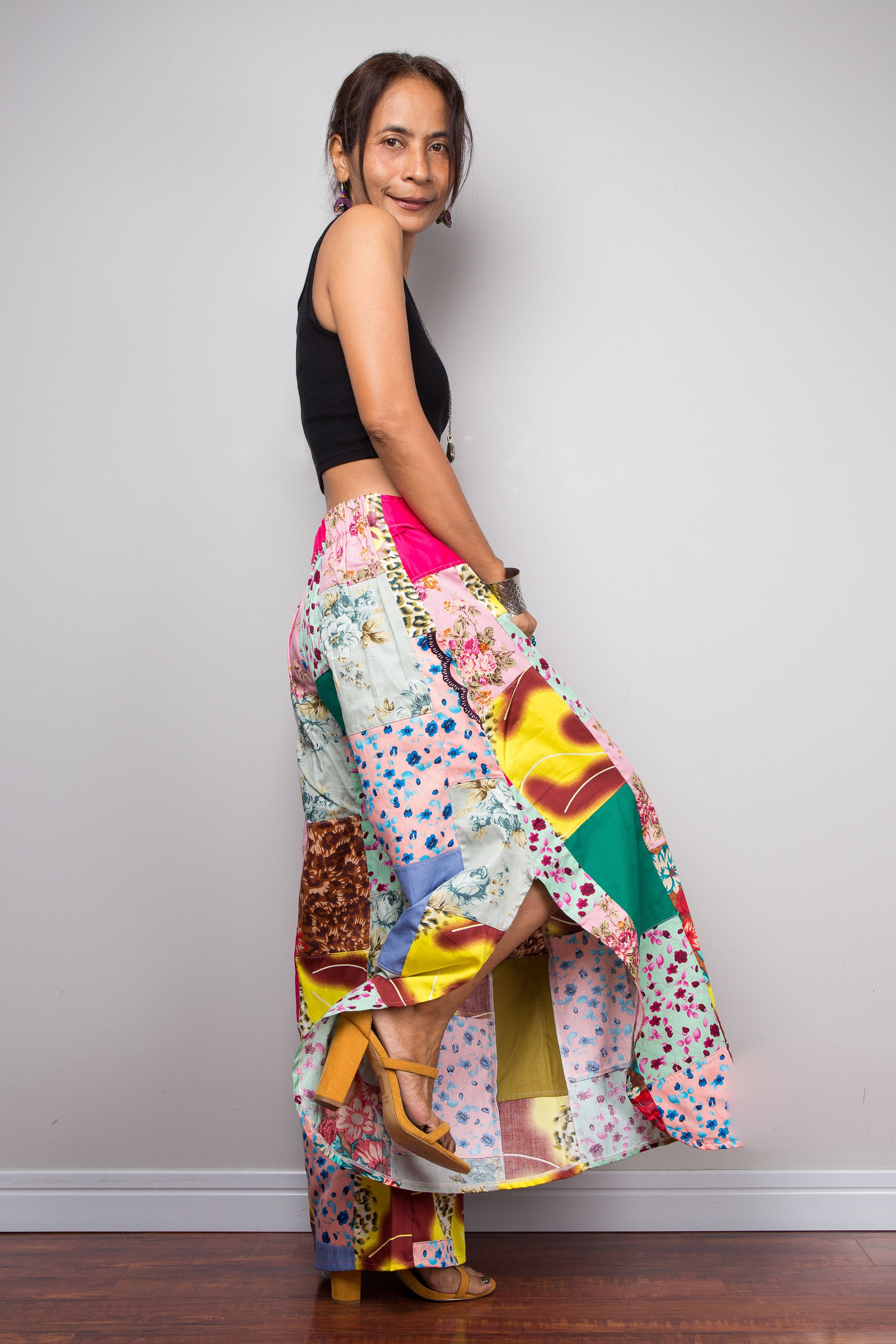 Full Side view of a model wearing the Nuichan pastel patchwork wide leg palazzo pants, full ultra-wide leg silhouette, and hand-sewn quilt-style patchwork construction in mixed cotton satin pastel prints including mint, blush pink, teal, yellow satin and floral panels, styled with a black crop top