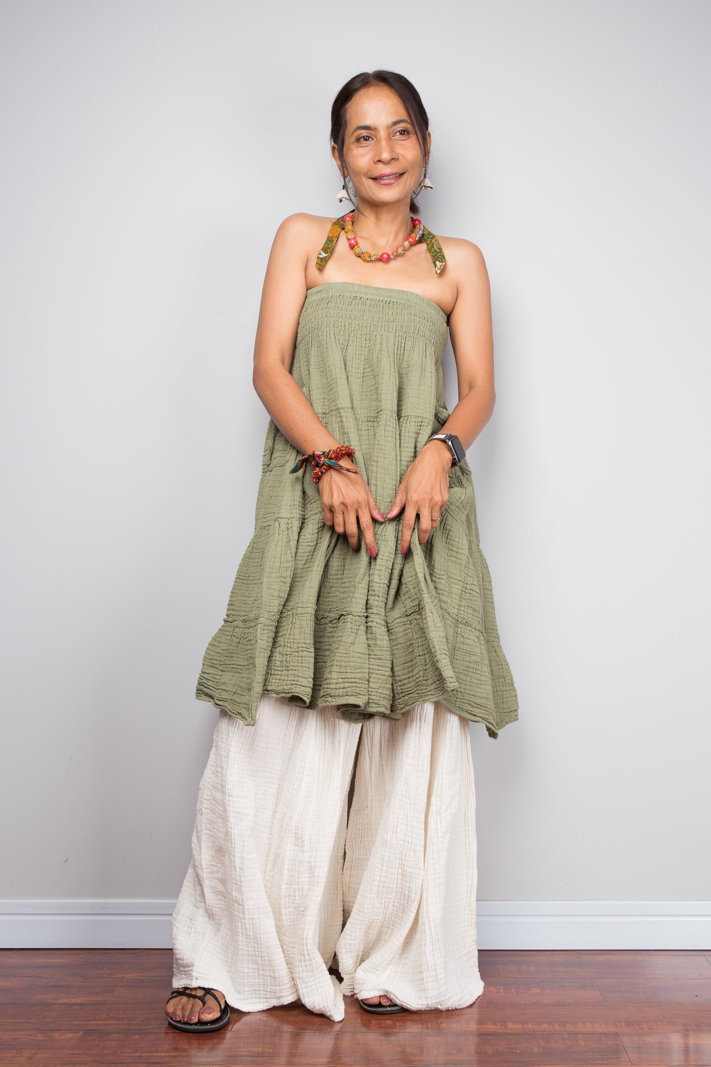 Woman wearing a green dress with cream cotton pants against a plain background