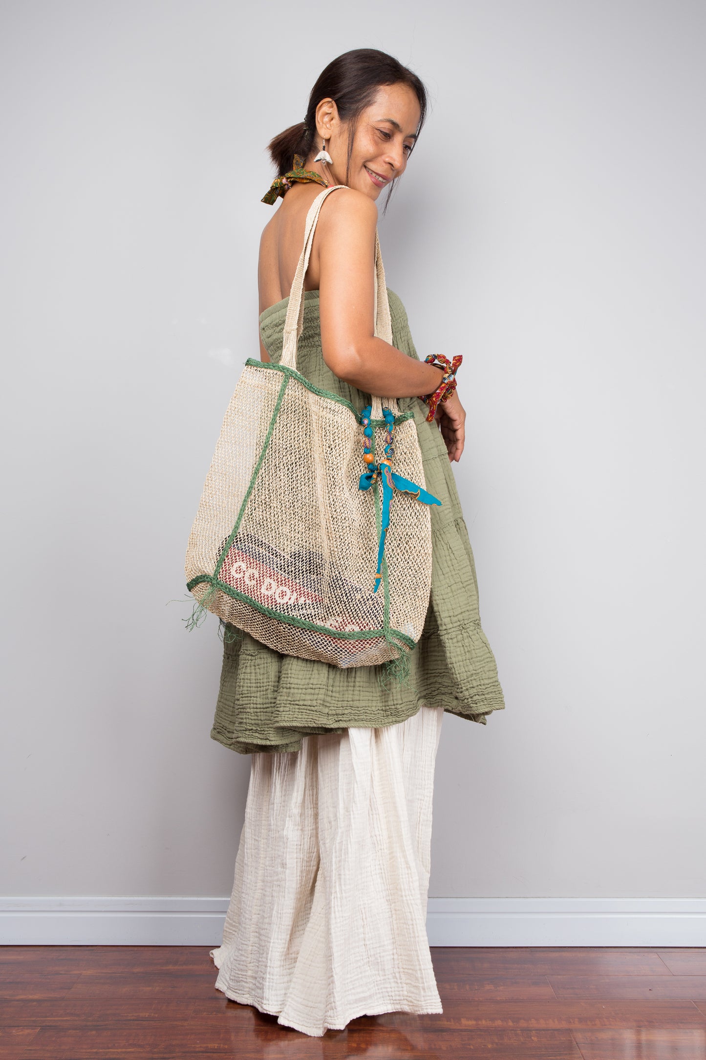 Woman holding a green and beige bag against a plain background