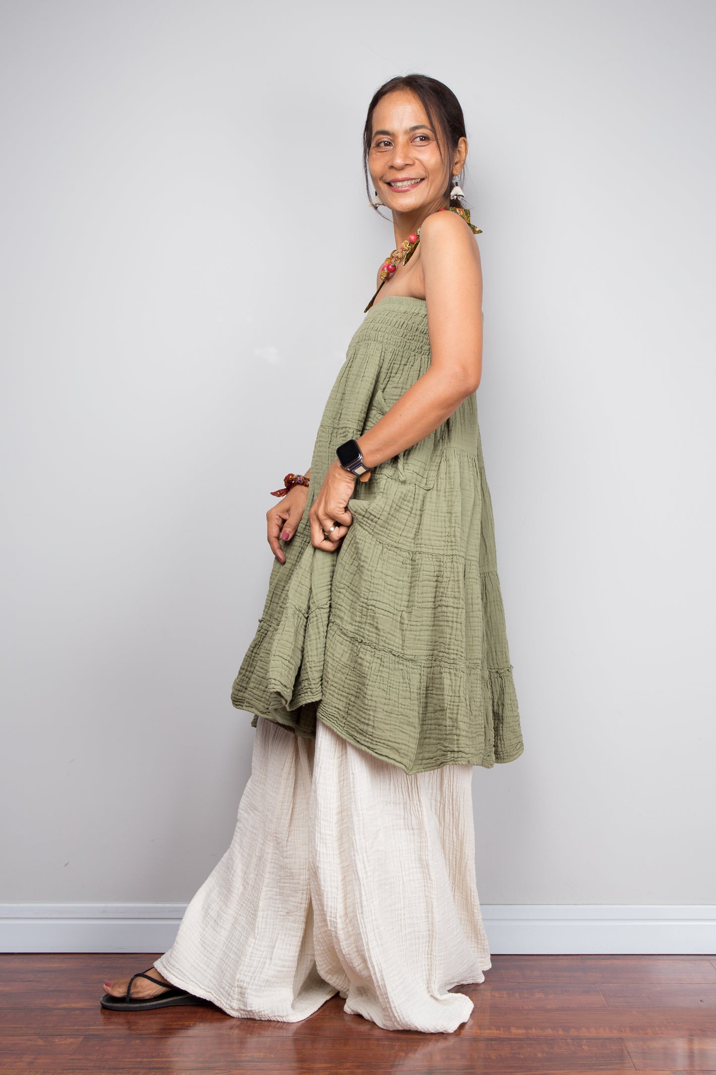 Woman wearing a green top and cream cotton wide leg pants against a plain background