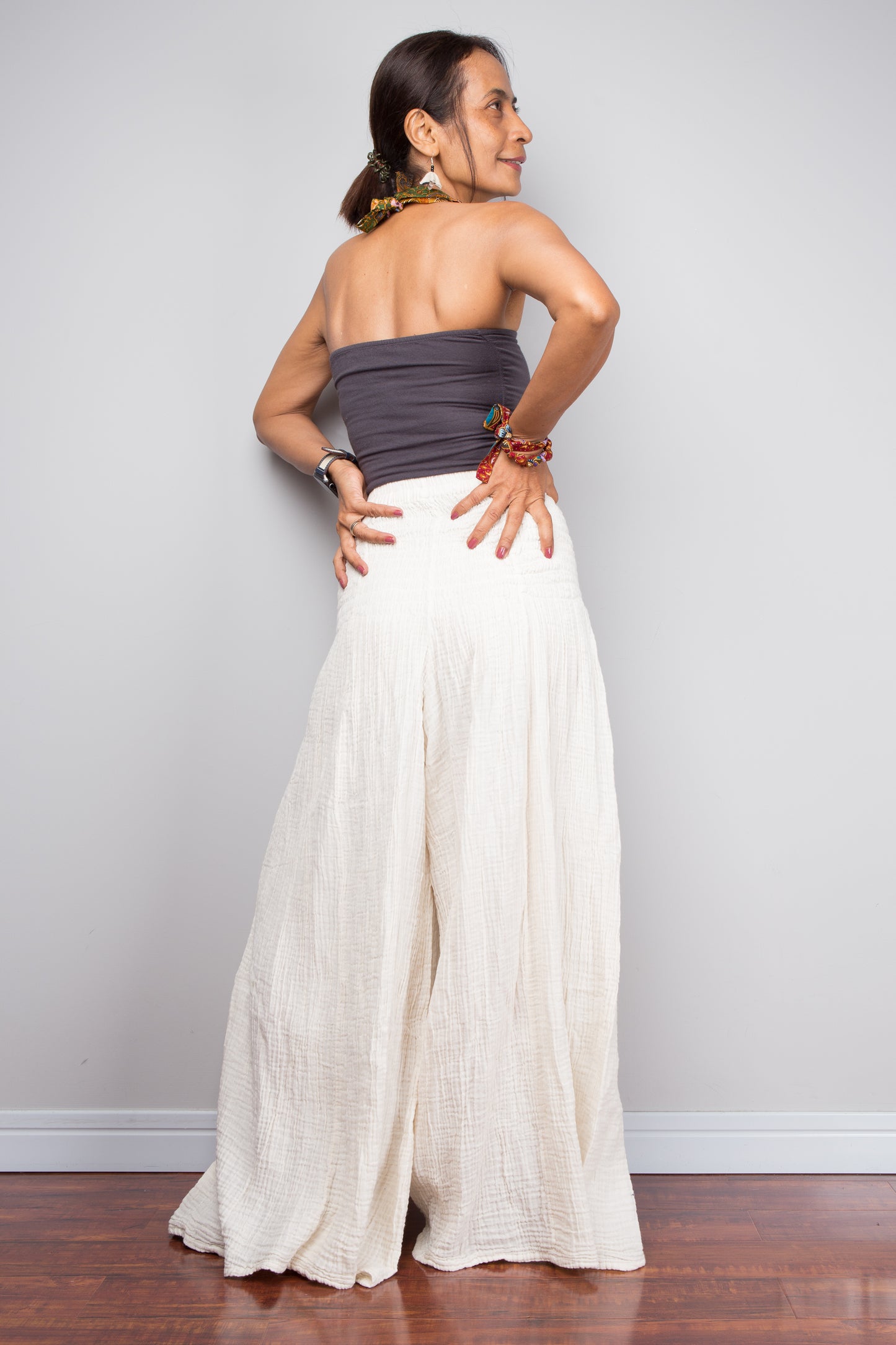 Woman wearing a strapless top and cream cotton pants against a plain background