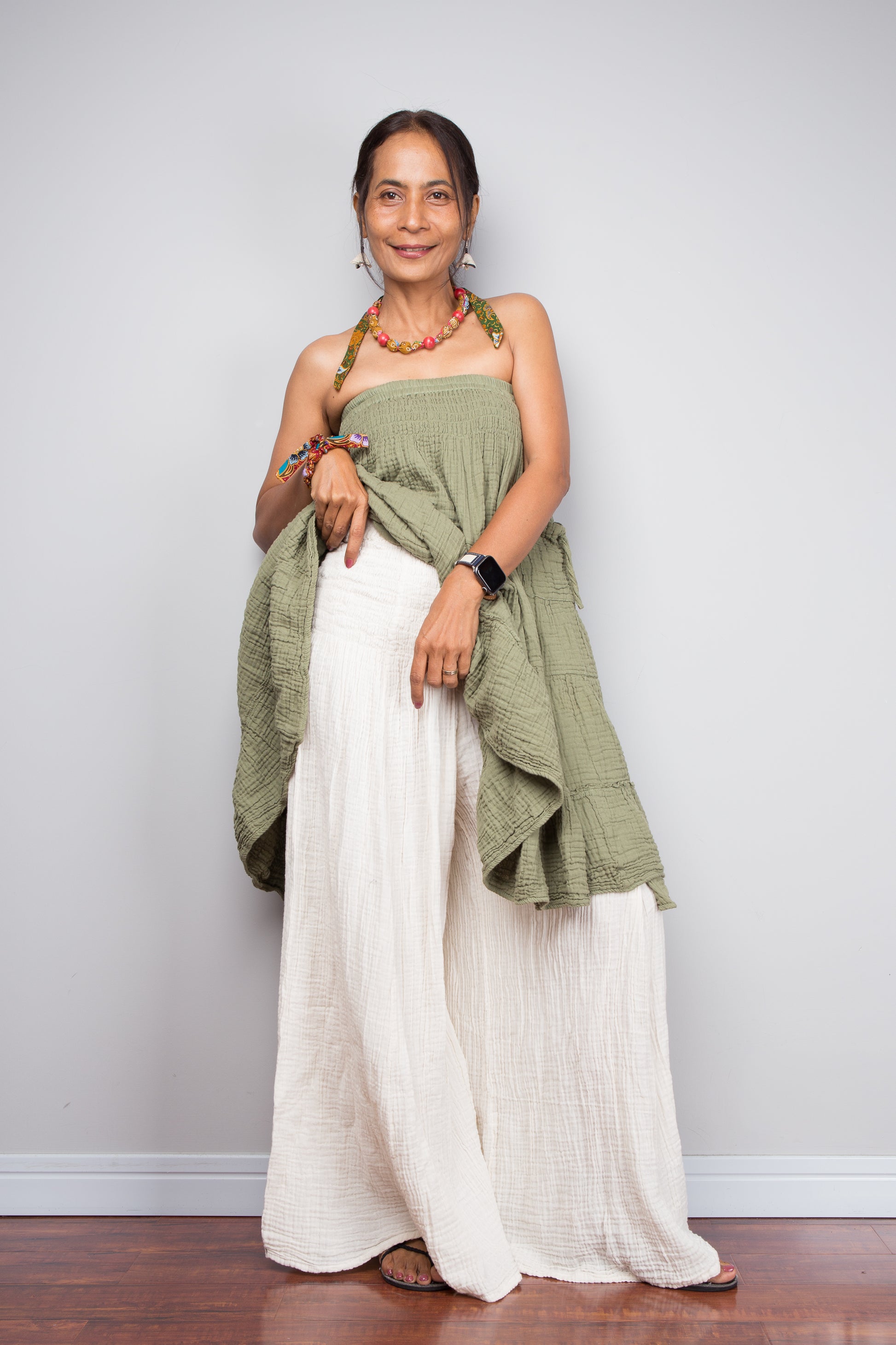 Woman wearing a green top and cream cotton pants against a plain background