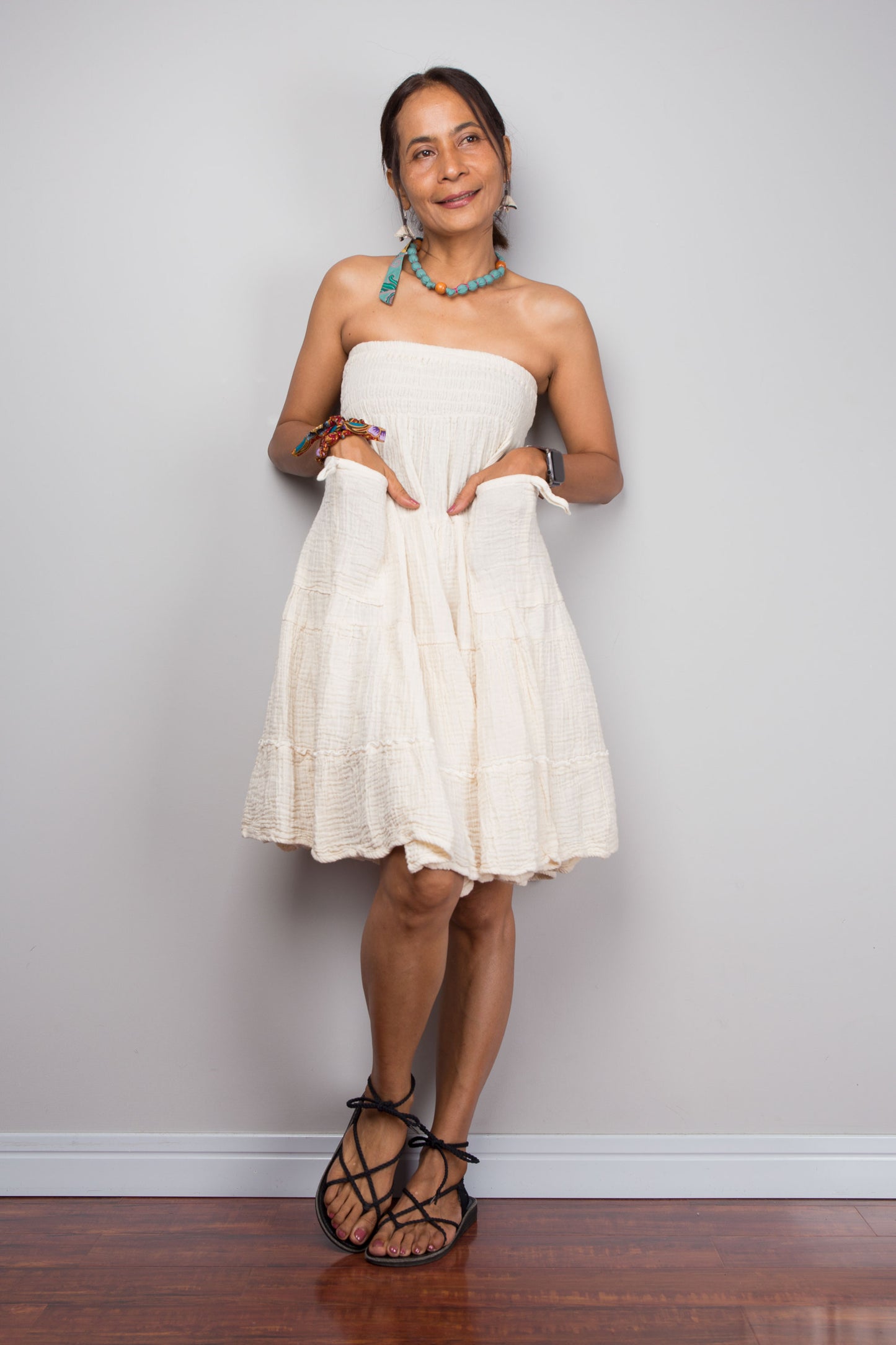Woman wearing a white strapless dress against a plain wall.