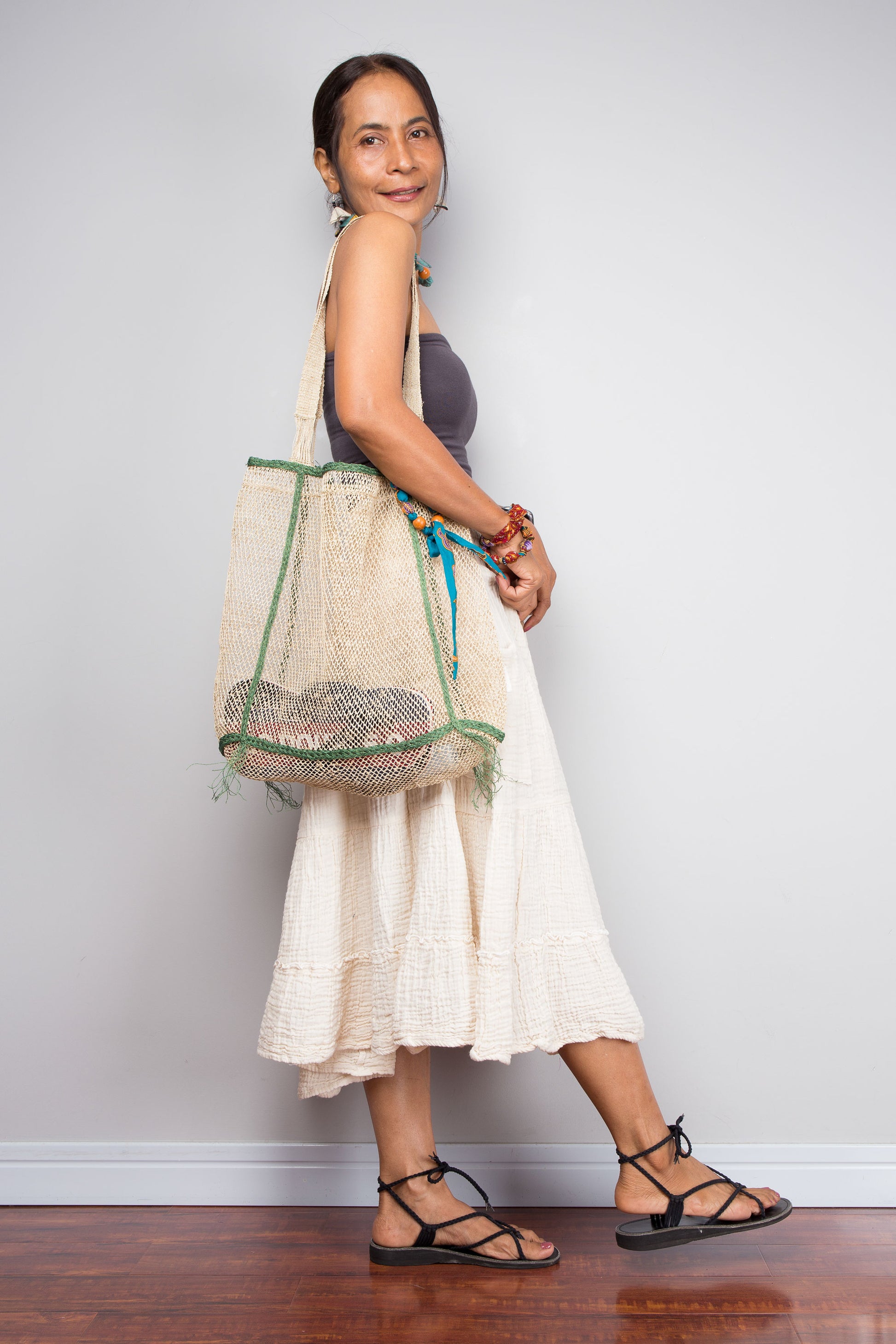 Woman holding a netted bag against a plain background