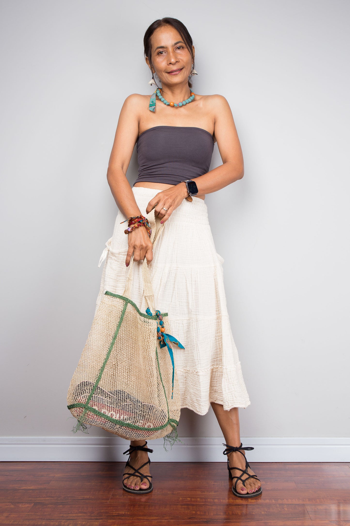 Woman wearing a strapless top and white skirt holding a net against a plain background
