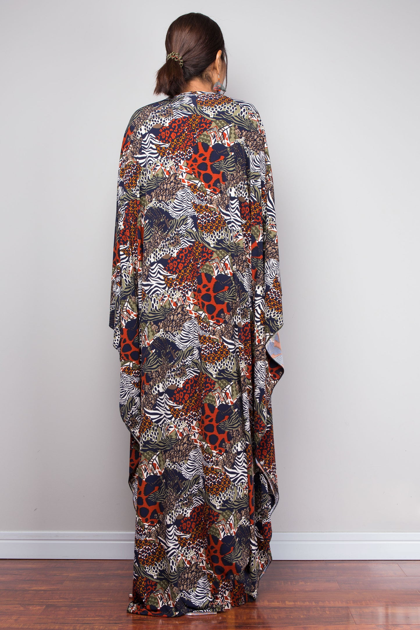 Woman wearing a long, patterned kaftan dress standing against a plain wall.