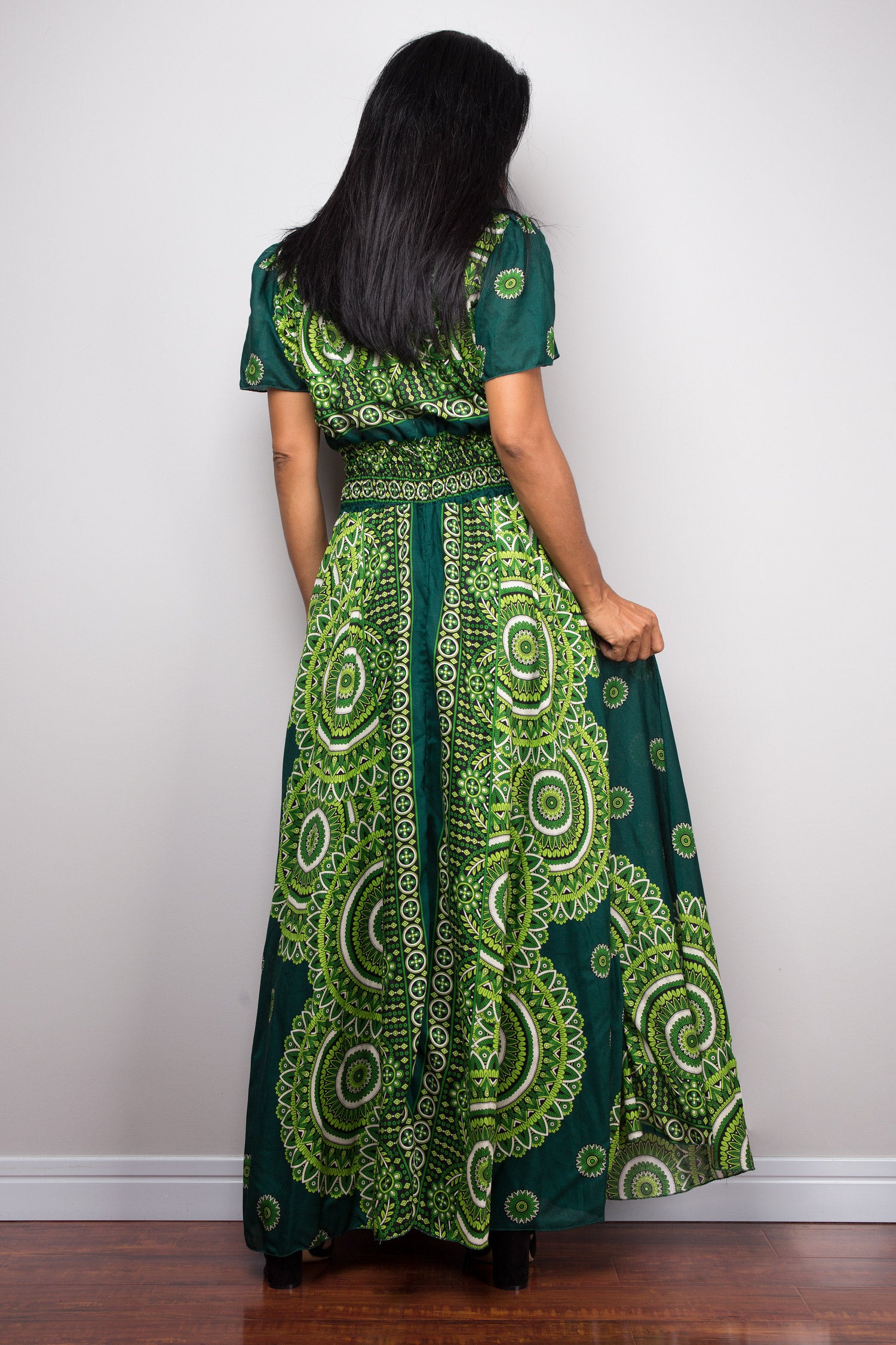 Person wearing a green patterned button dress against a white wall.