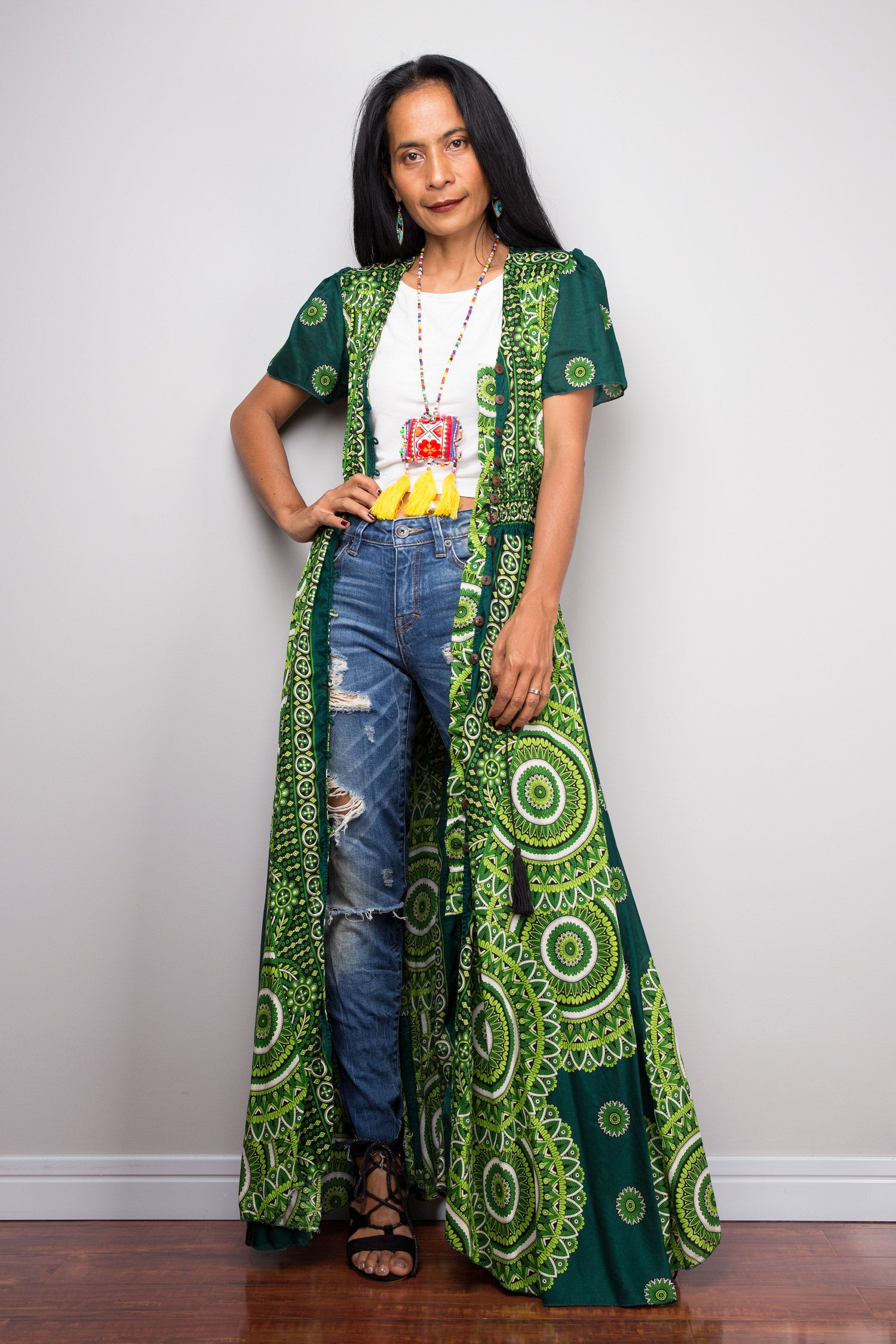 Woman wearing a long green patterned dress over jeans against a white background.  Nuichan button dress for summer